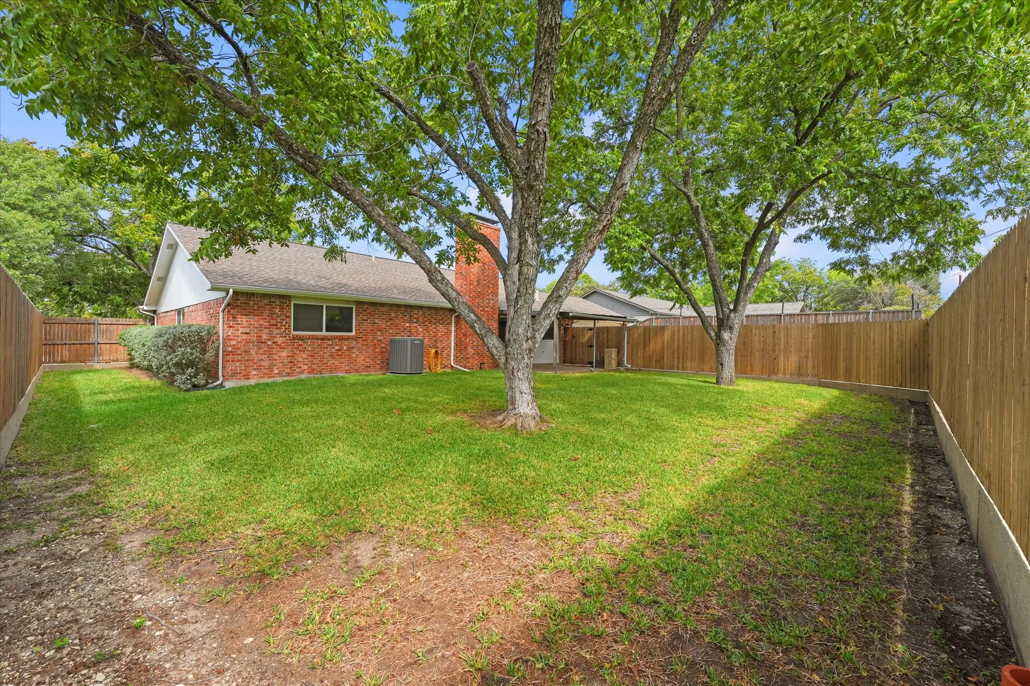 Expansive backyard featuring a brick exterior, mature trees, wood privacy fencing, and a red brick chimney