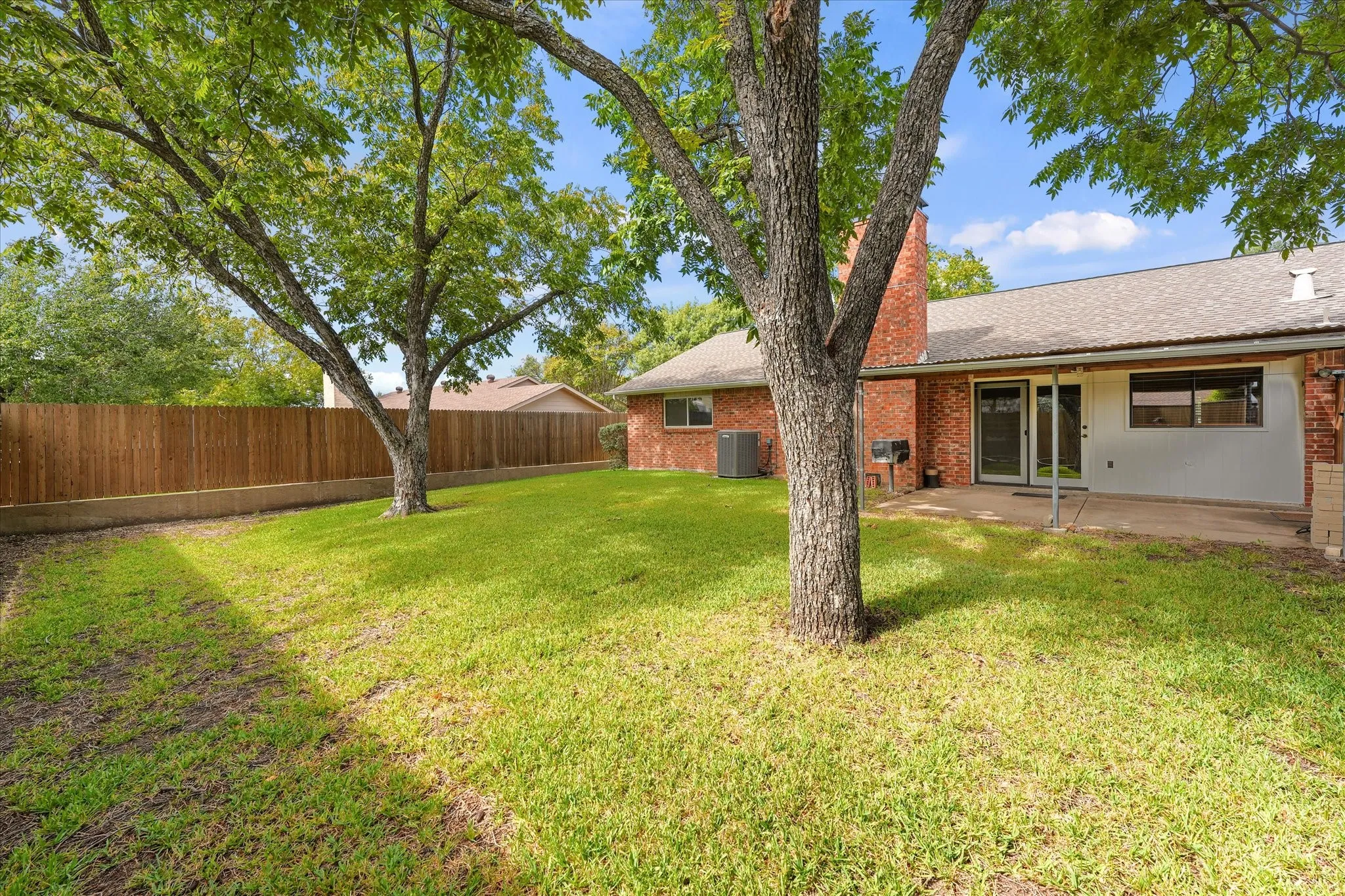 Large backyard featuring mature trees, a brick chimney, covered patio and wood-style privacy fencing.