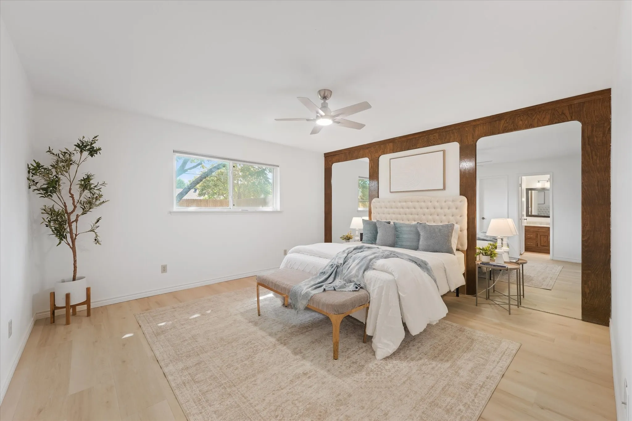 Large primary bedroom with wood-finish LVP flooring, custom wood-paneled accent wall with integrated mirrors, and new LED ceiling fan with 3 light tone options.