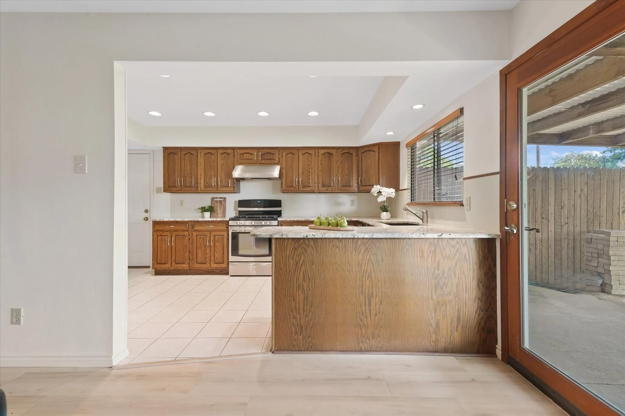 Kitchen featuring wood cabinetry, granite countertops, stainless steel appliances, recessed lighting with dimmer, and tile flooring, view into large private backyard.