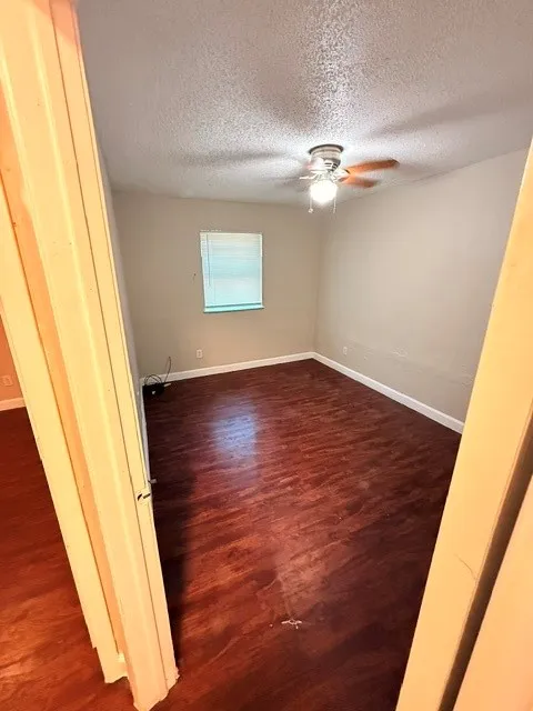 Wood-finish flooring with baseboard trim, neutral wall tones, and window with blinds