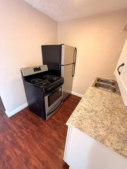 Full-size stainless steel refrigerator, stainless steel range, wood-finish flooring, dual basin sink, and laminate countertop