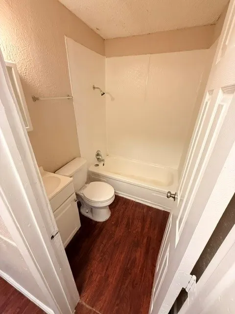 White tub and shower combination with a single-handle faucet, vanity with integrated sink, and wood-finish flooring