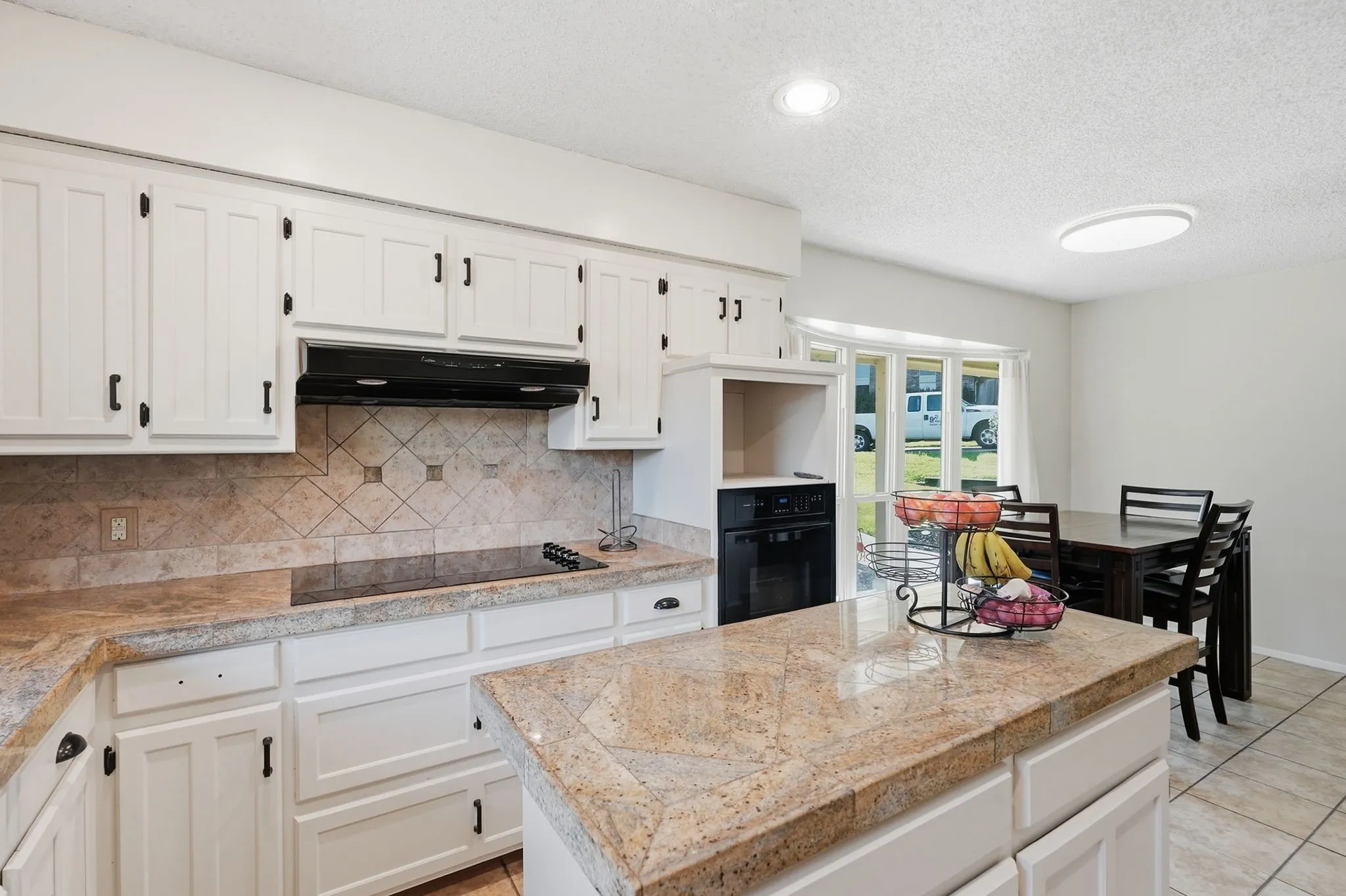 White cabinetry with black hardware, stone countertops, tiled backsplash, integrated cooktop, and a built-in oven