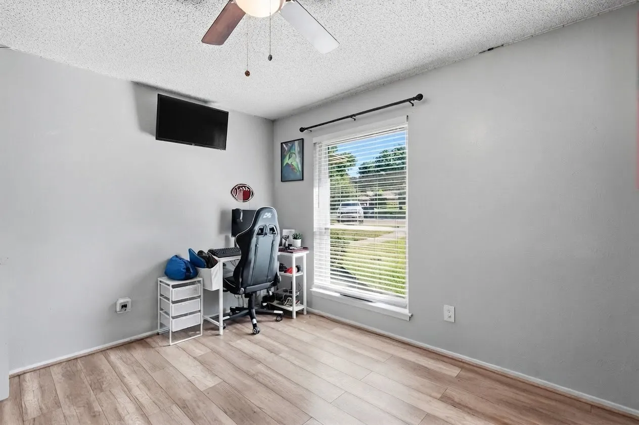 Wood-finish flooring, light gray wall paint, window with blinds, and ceiling fan with light fixture