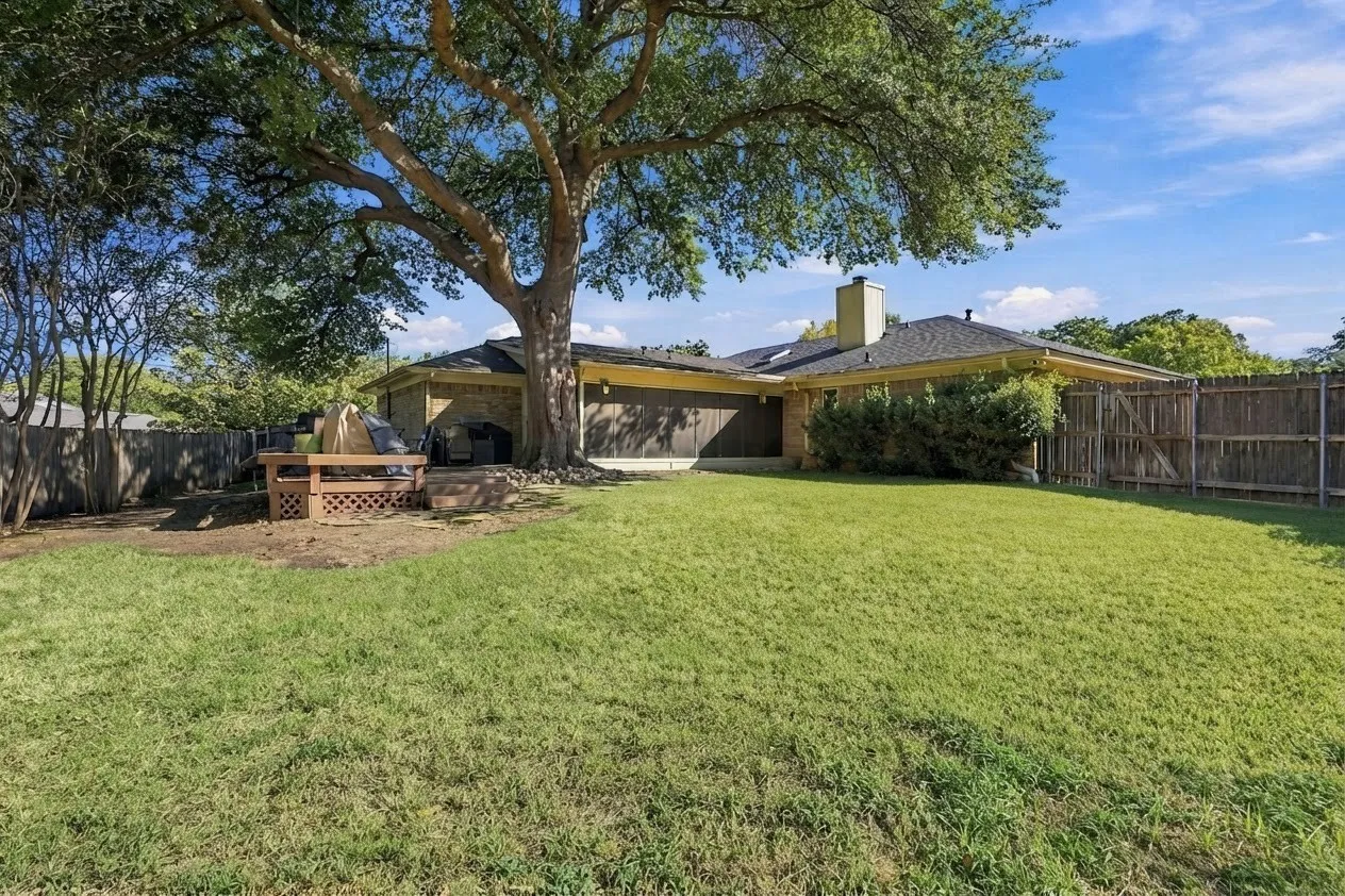 Expansive lawn with mature trees and perimeter fencing, featuring a wood deck patio