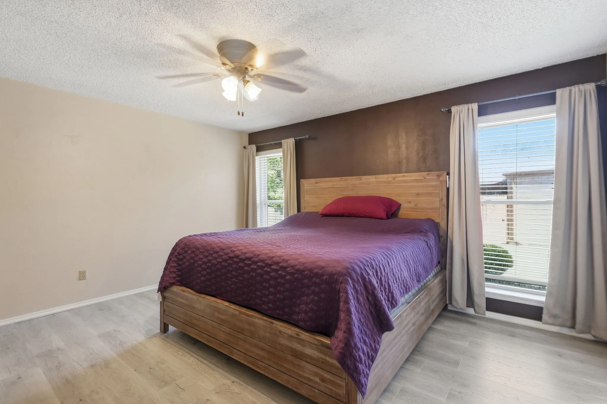 Light wood-finish flooring with a ceiling fan, dual windows, and neutral wall tones