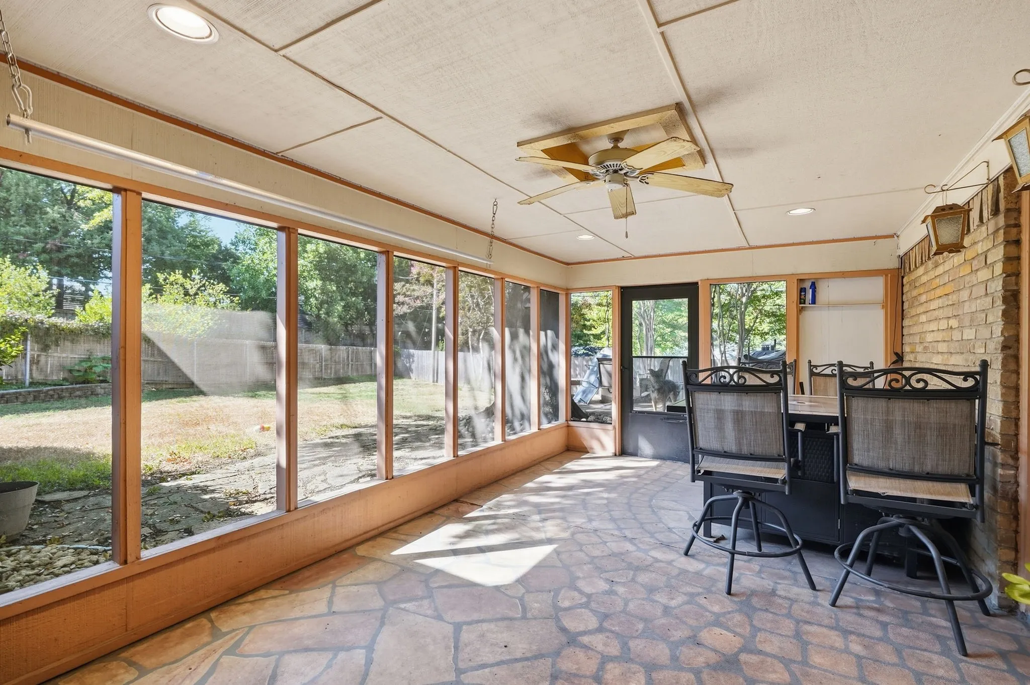 Screened-in porch featuring a flagstone-style floor, exposed brick wall, ceiling fan, and recessed lighting