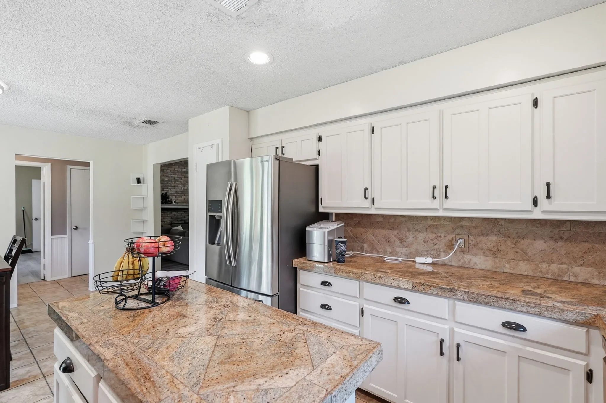 White shaker cabinetry with dark hardware, stone-finish countertops, tile backsplash, and recessed lighting