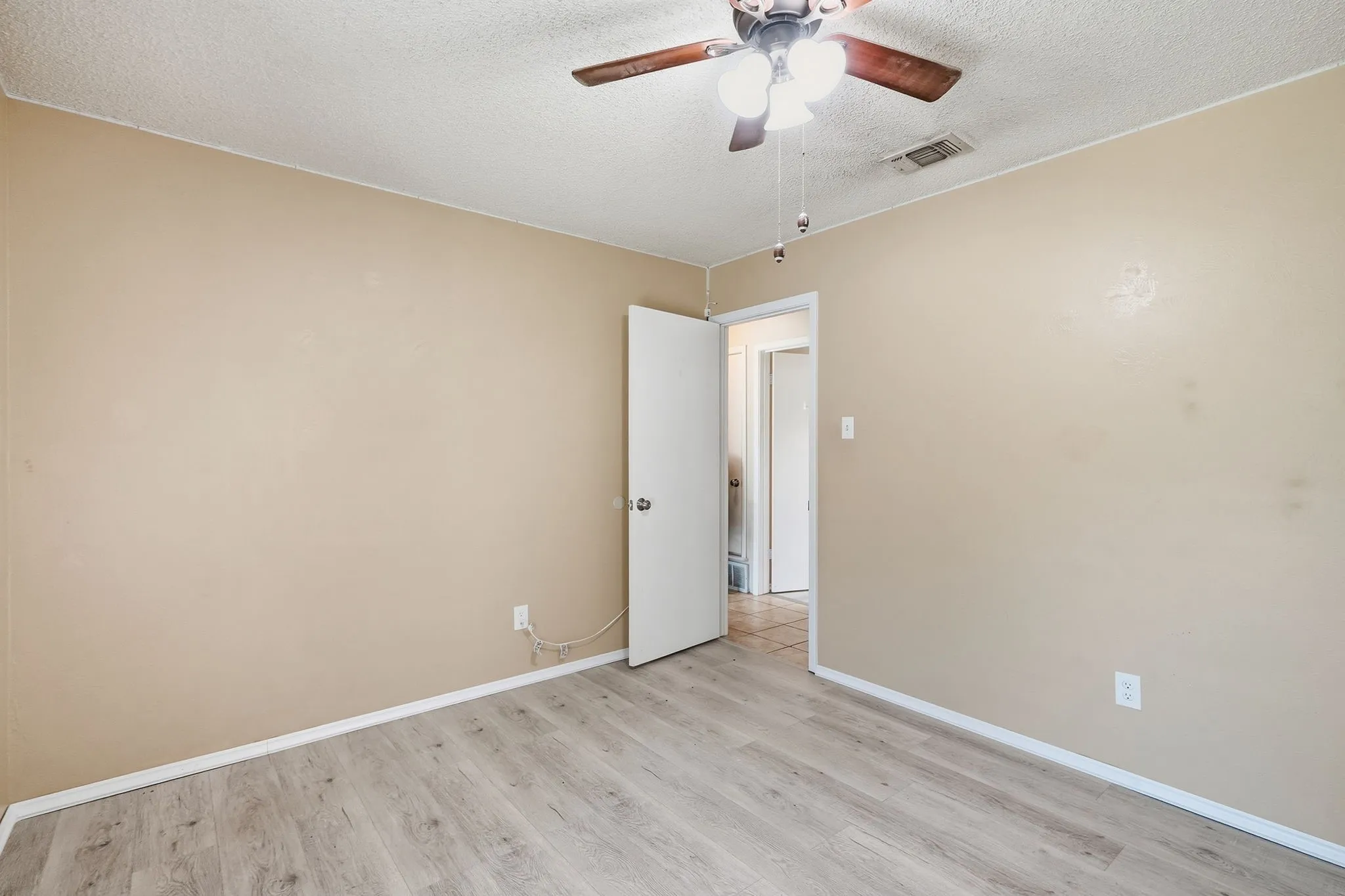 Neutral-toned walls, wood-finish flooring, ceiling fan with light fixture, white trim, and a white interior door