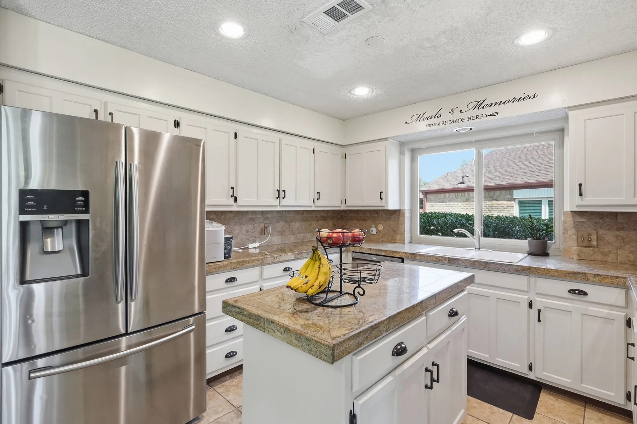 White cabinetry with black hardware, stainless steel refrigerator, stone countertops, and recessed lighting