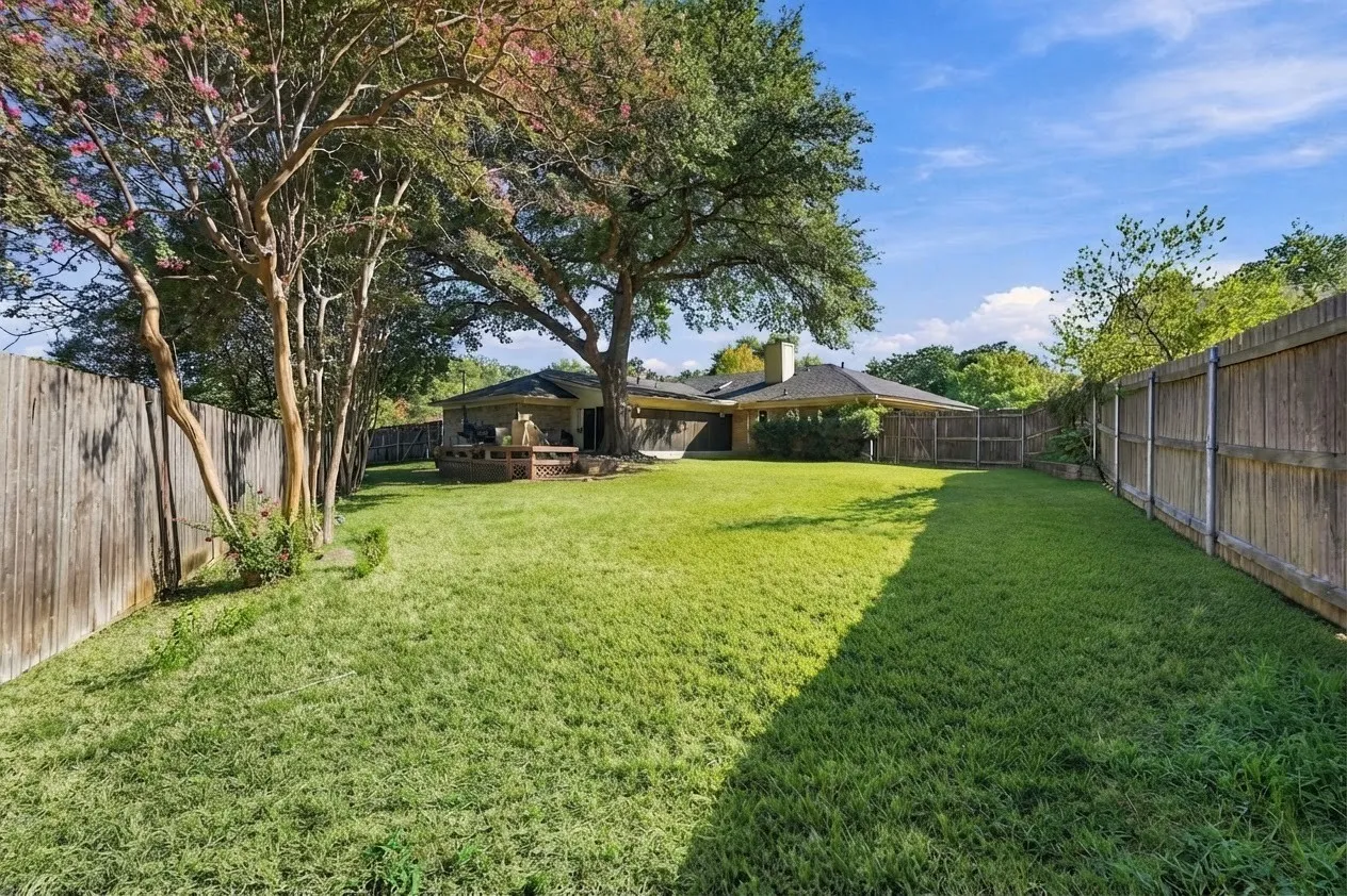 Expansive backyard with a manicured lawn, established trees, and perimeter fencing