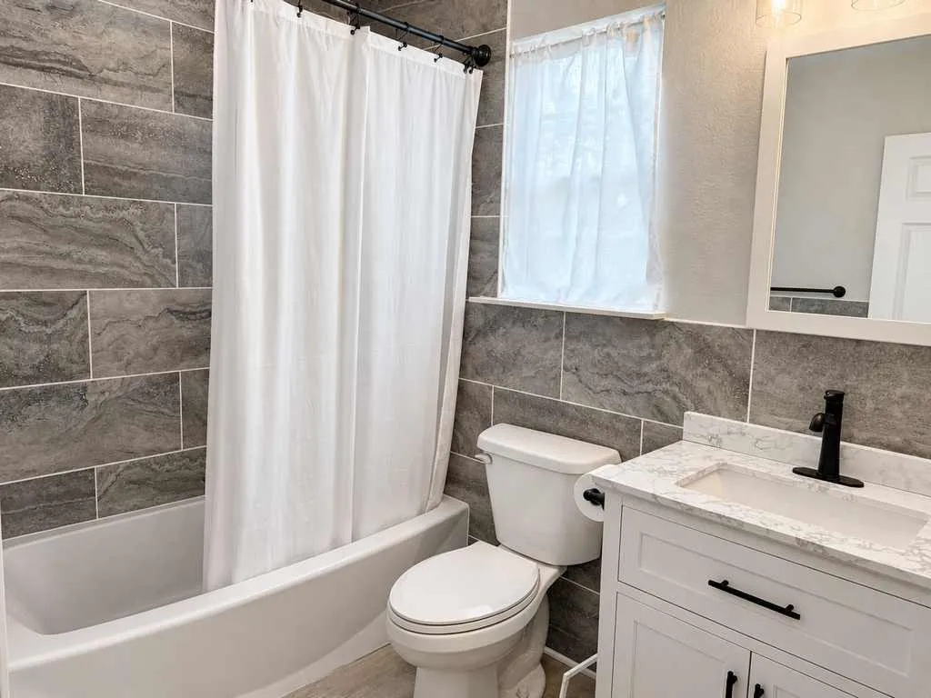 Tiled tub/shower surround, vanity with stone-look countertop and contrasting black fixtures.