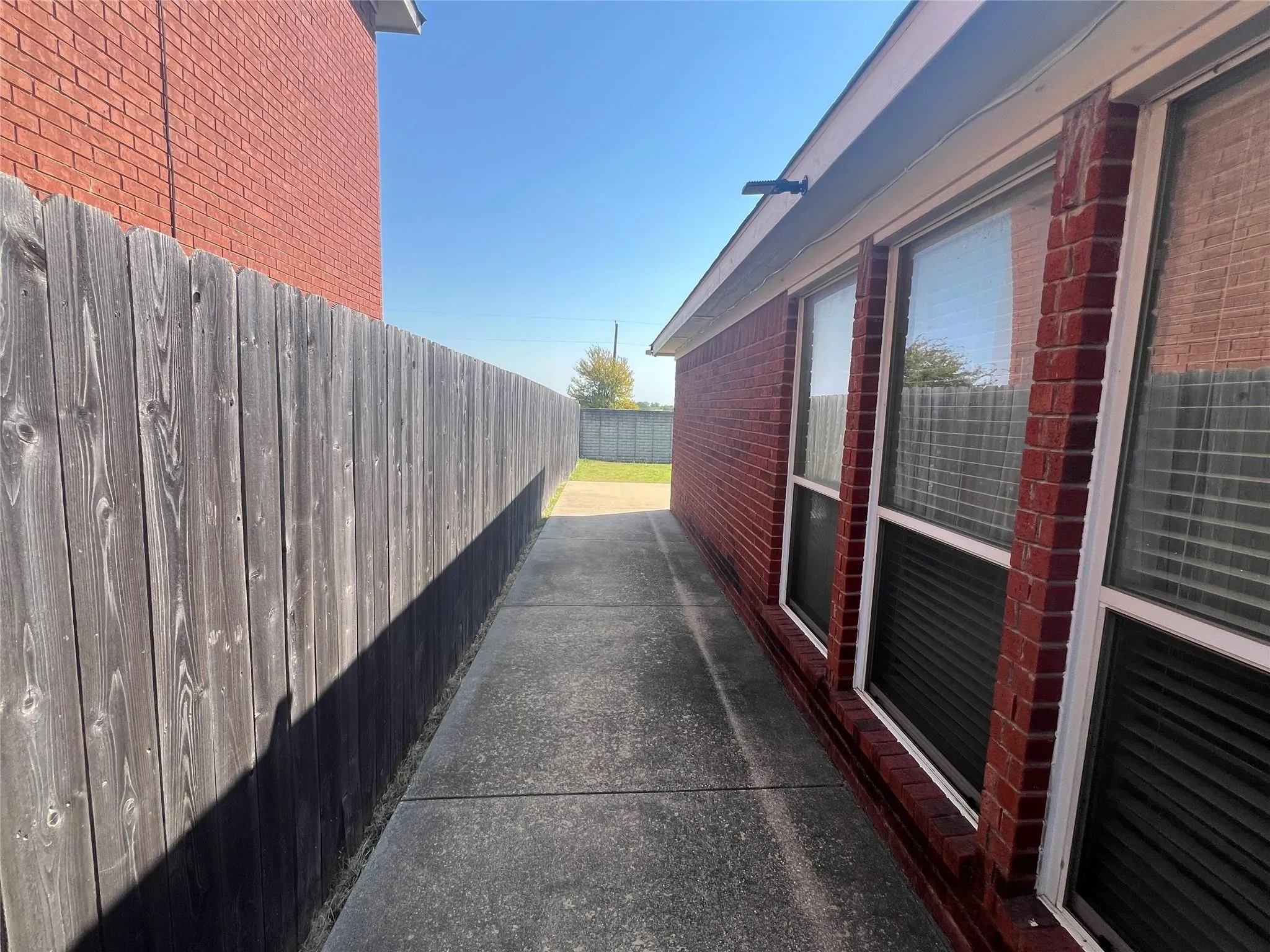 Red brick exterior with multiple windows, concrete walkway, and a wooden fence