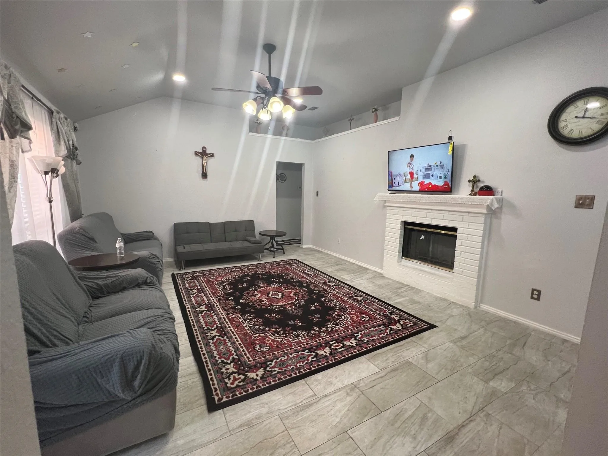 Vaulted ceiling with recessed lighting, fireplace with white brick surround, ceiling fan with integrated lighting, and light-toned tile flooring