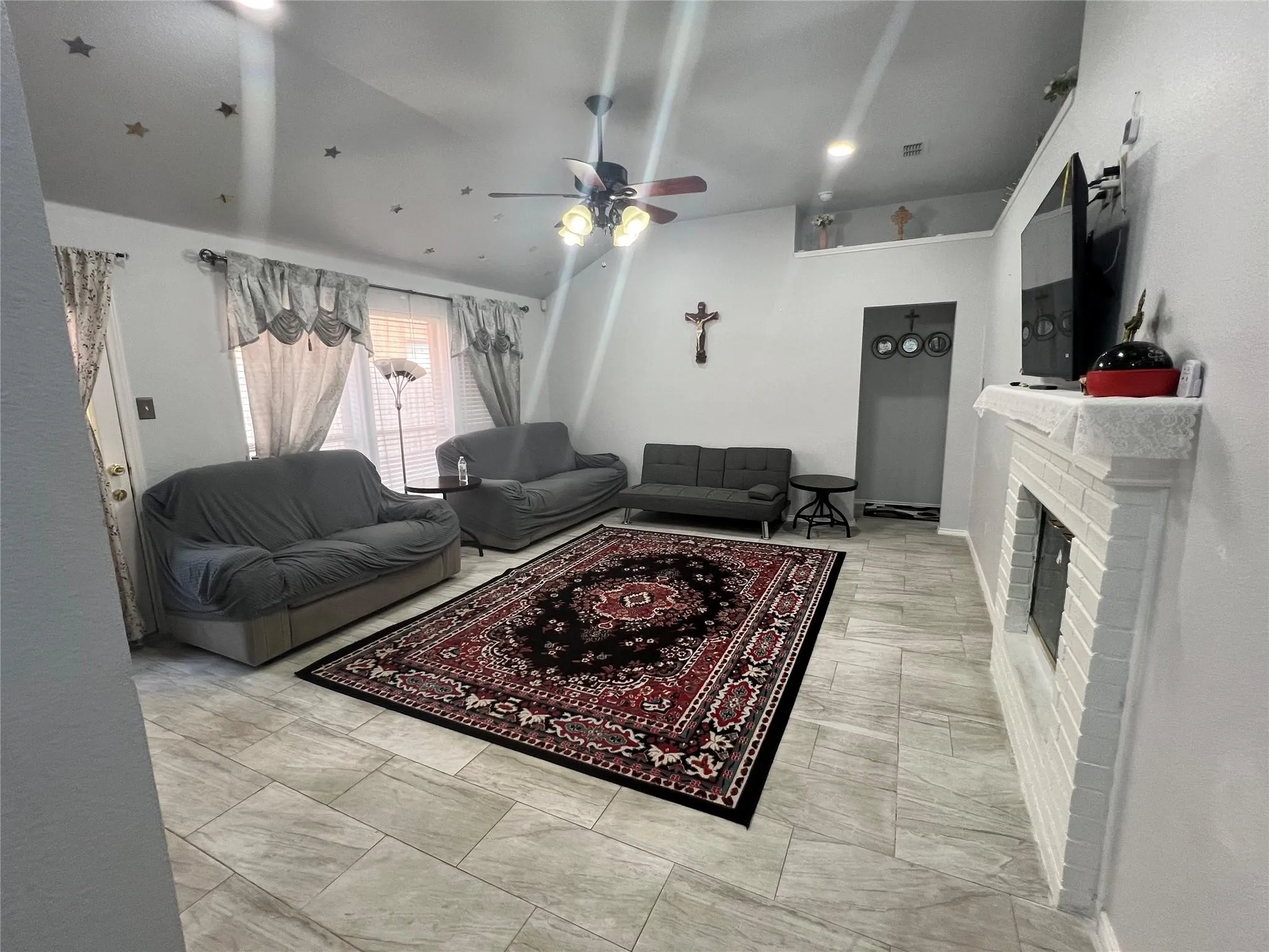 Spacious living area featuring light-toned tile flooring, a painted brick fireplace, a vaulted ceiling, and recessed lighting