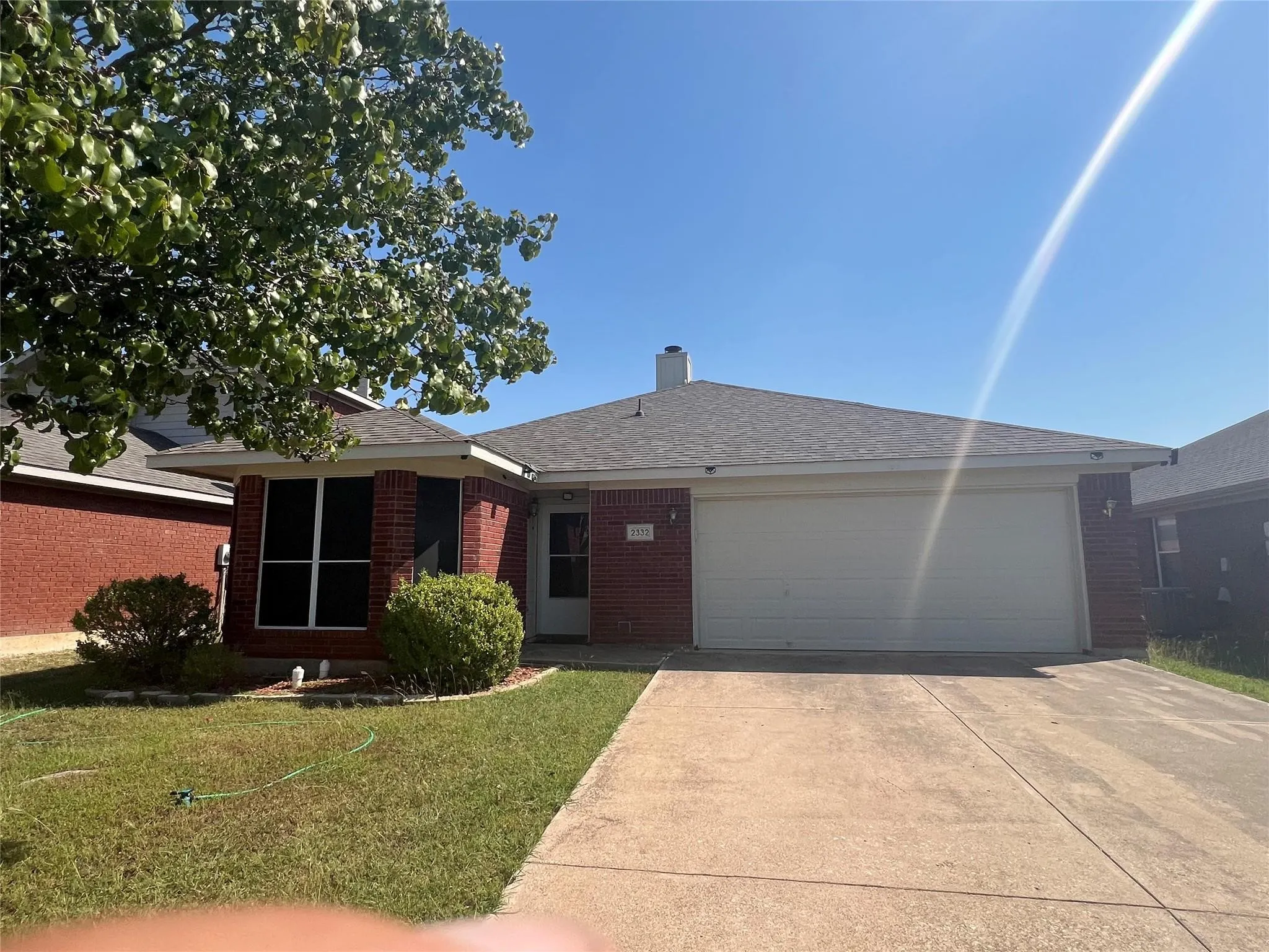 Brick exterior with a gray shingle roof, attached garage, concrete driveway, and front lawn landscaping