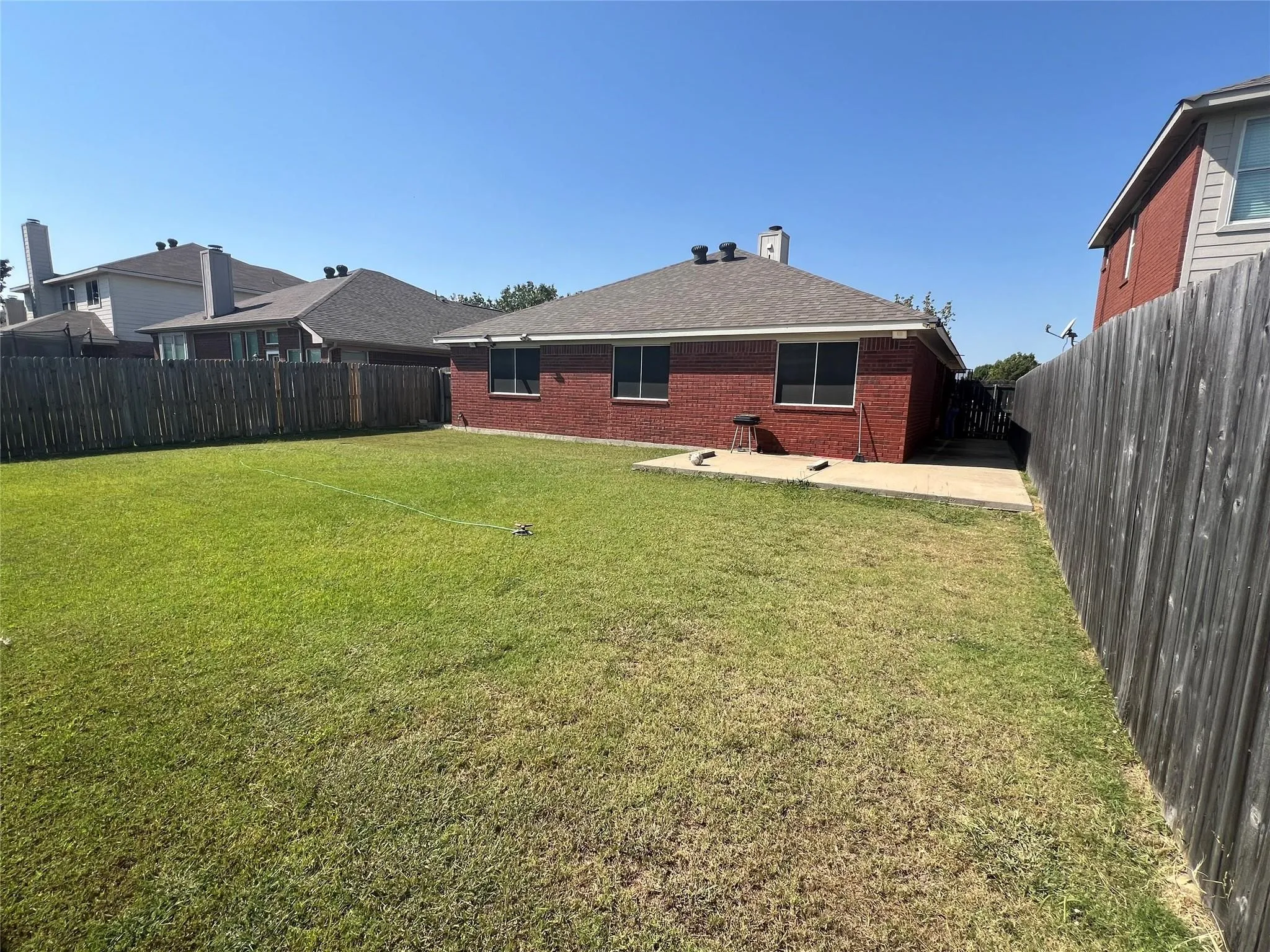 Expansive grassy yard with a concrete pathway leading to the home's red brick exterior, featuring multiple windows and a shingled roof