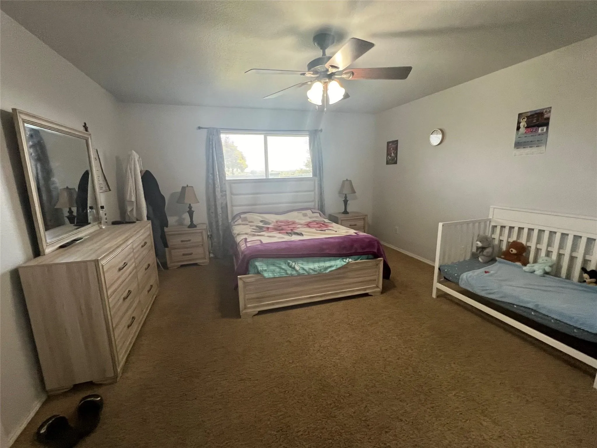 Carpeted room with a ceiling fan, light-toned walls, and a window with drapery