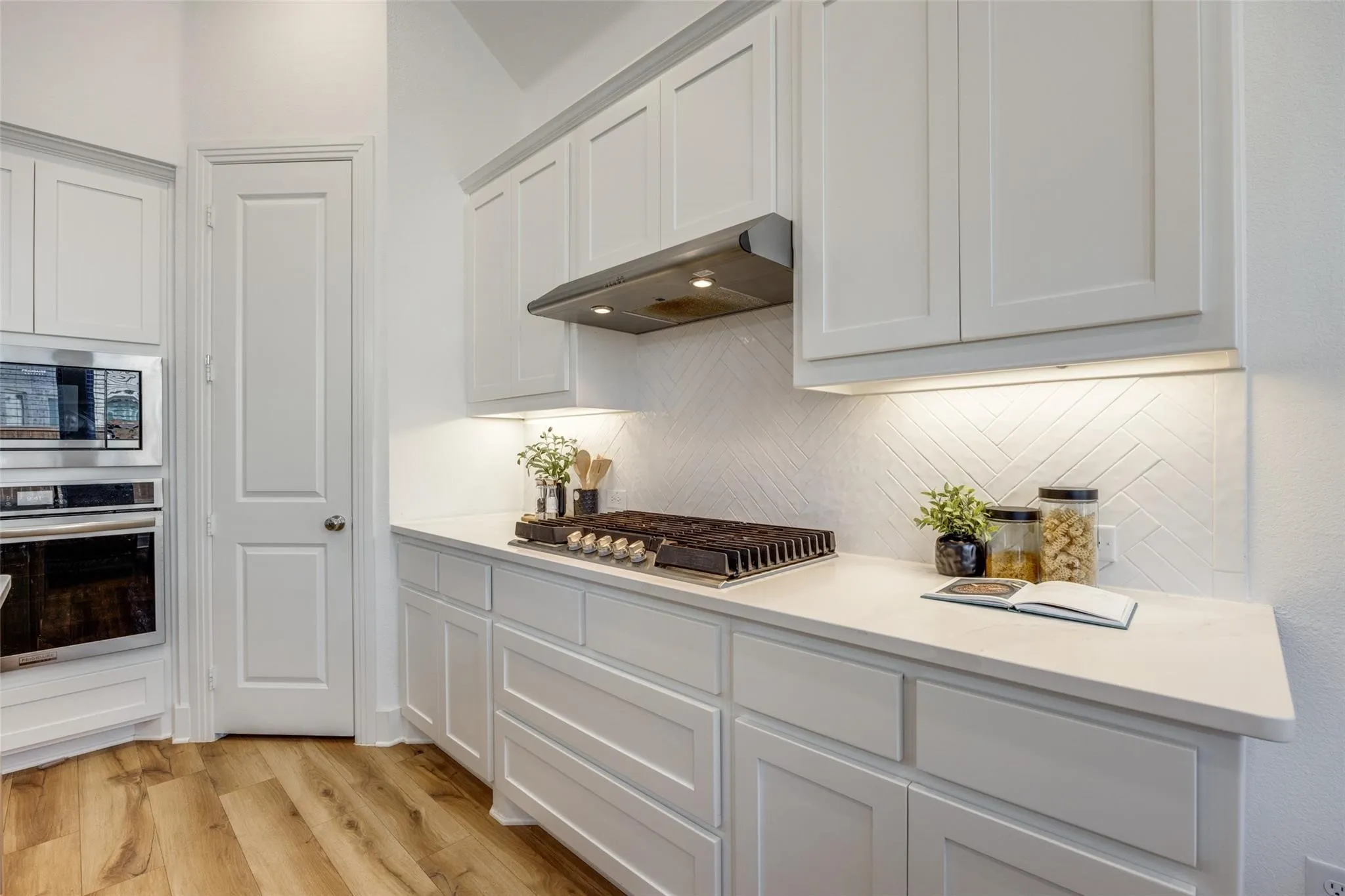 Kitchen with stainless steel appliances, under cabinet range hood, decorative backsplash, light wood finished floors, and light countertops