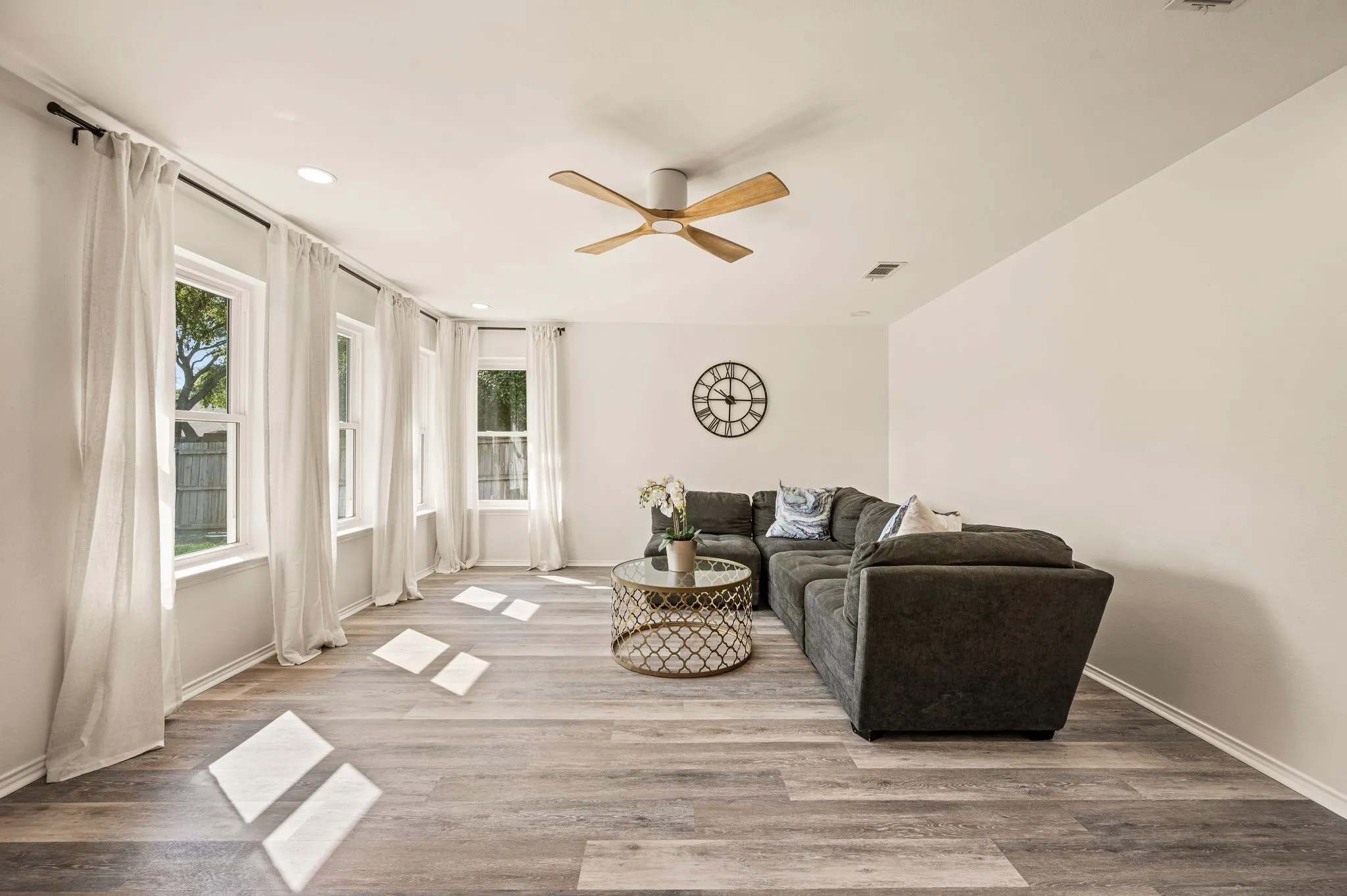 Light wood-finish flooring with recessed lighting and a ceiling fan