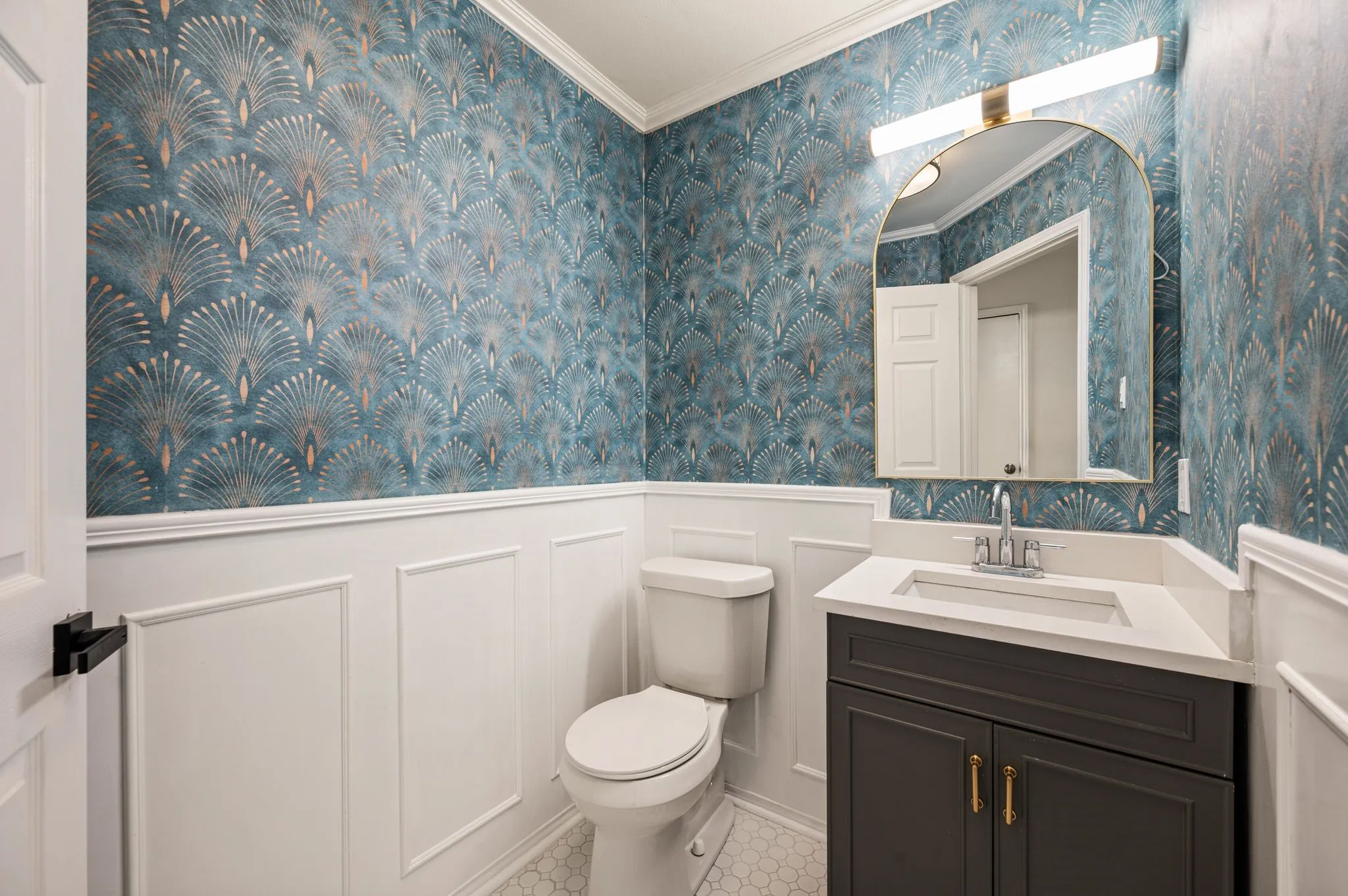 Powder room with patterned wall covering, white wainscoting, a single vanity with dark cabinetry, and a white countertop