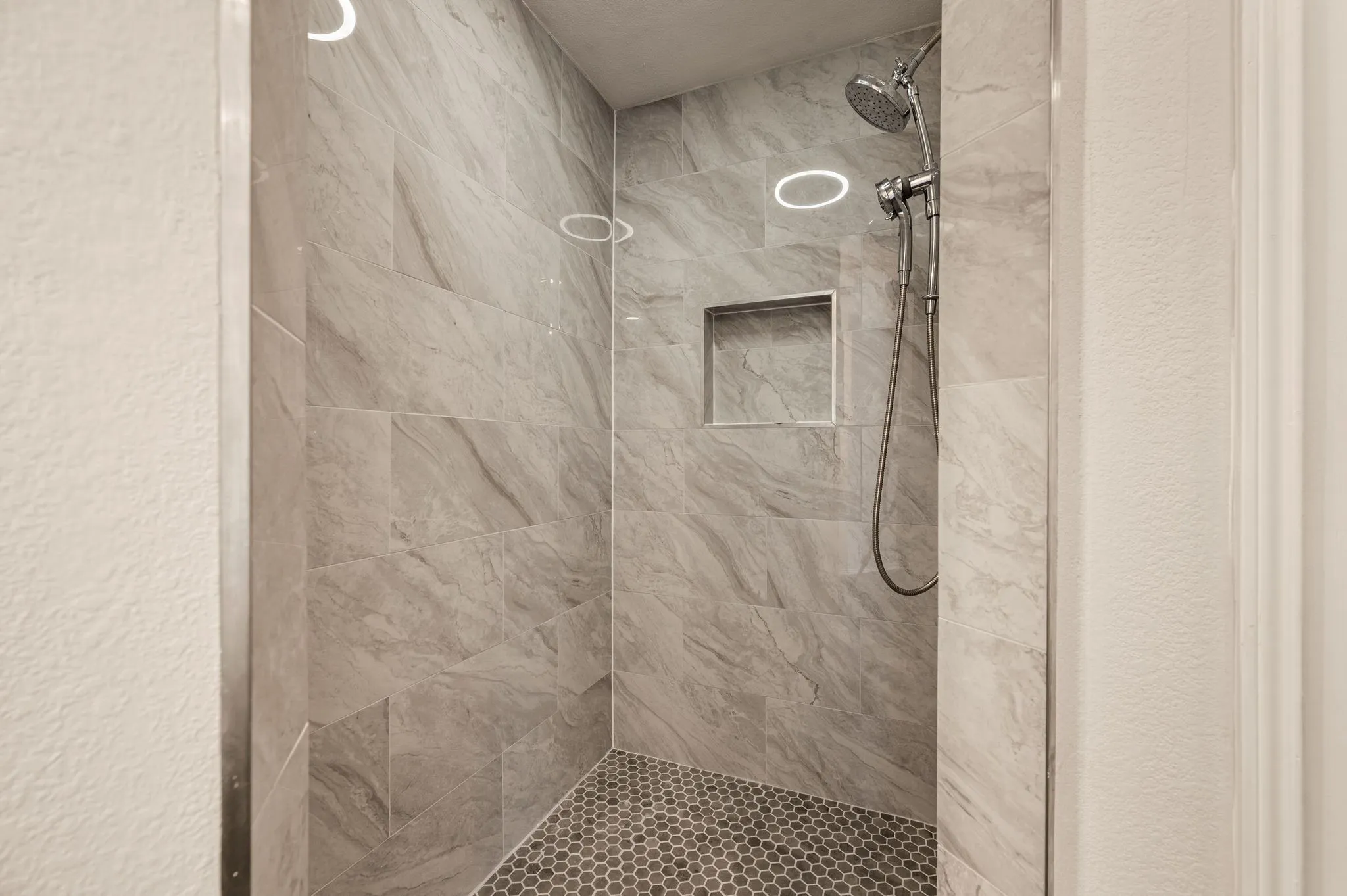 Walk-in shower with large-format wall tiles, hexagonal floor tiles, built-in niche, and a chrome shower fixture