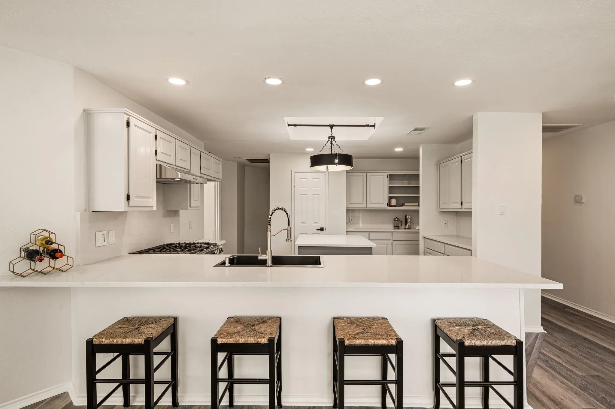 Expansive kitchen island with a built-in sink, recessed lighting, white cabinetry, and wood-finish flooring