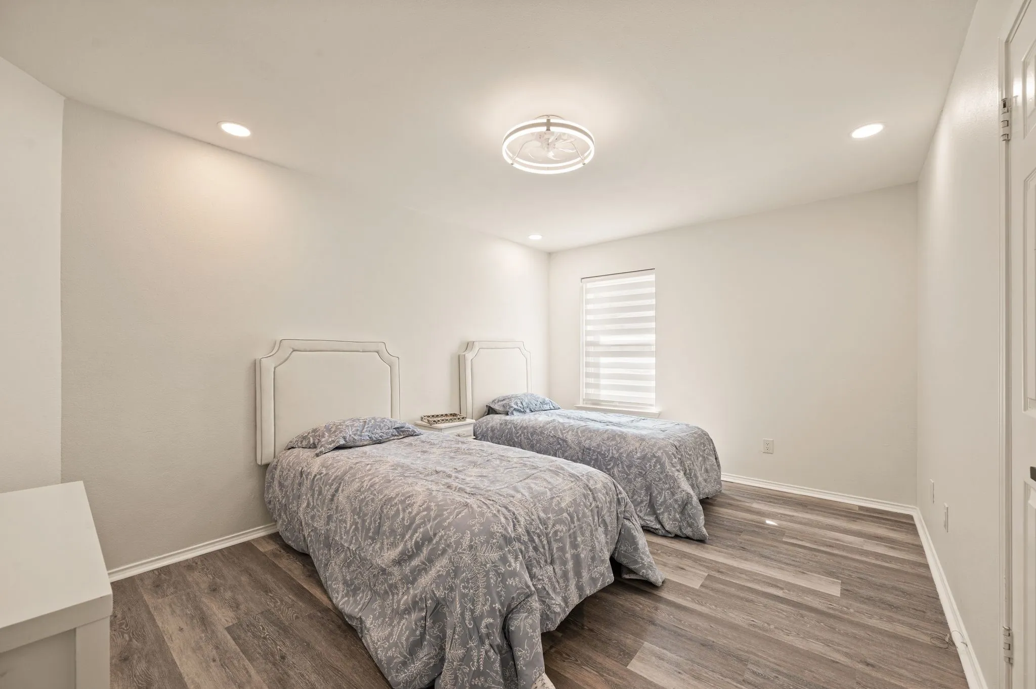Recessed lighting, central ceiling fixture, wood-finish flooring, and window with blinds