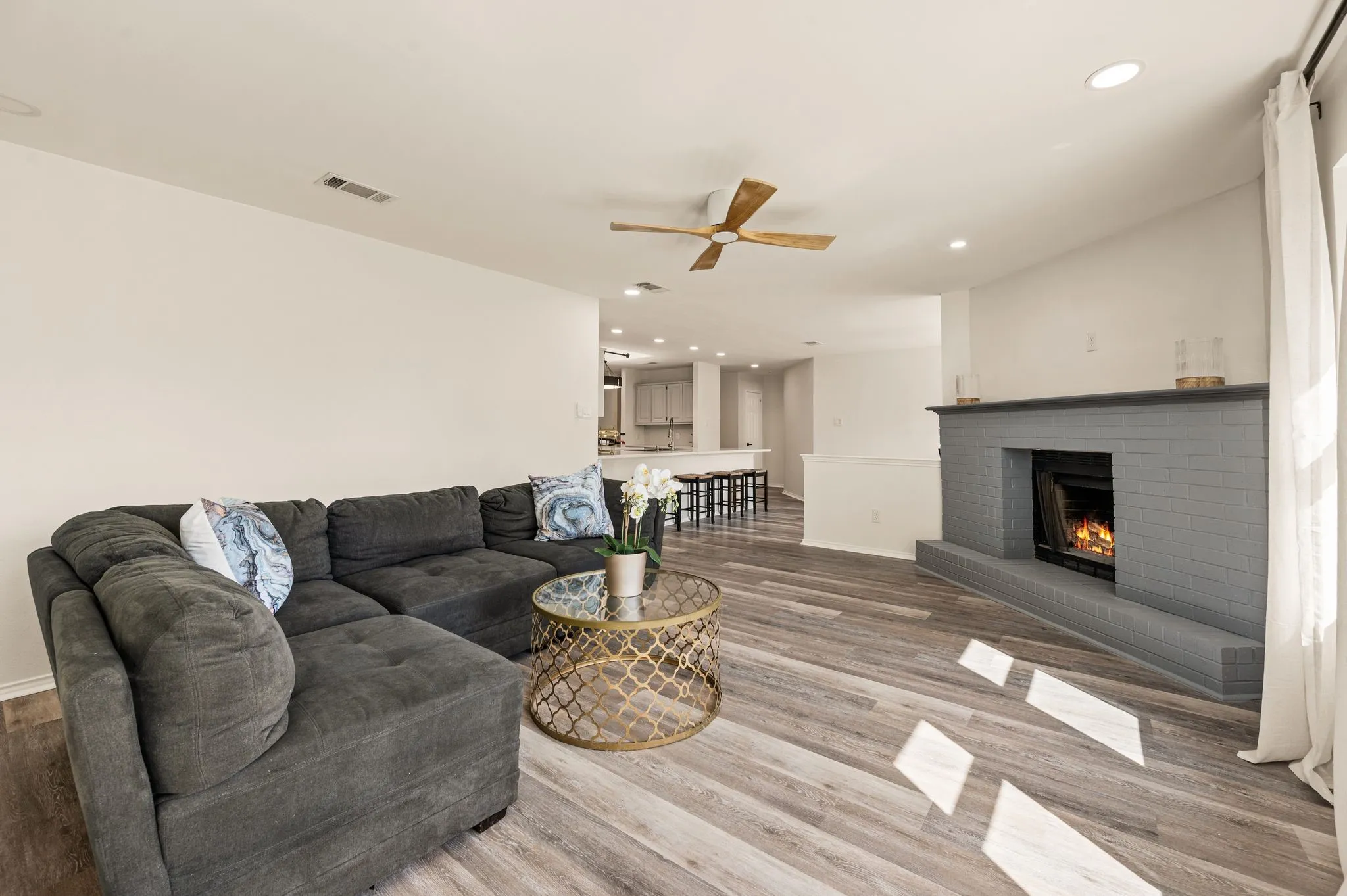 Spacious living area featuring wood-finish flooring, a painted brick fireplace, a ceiling fan, and recessed lighting