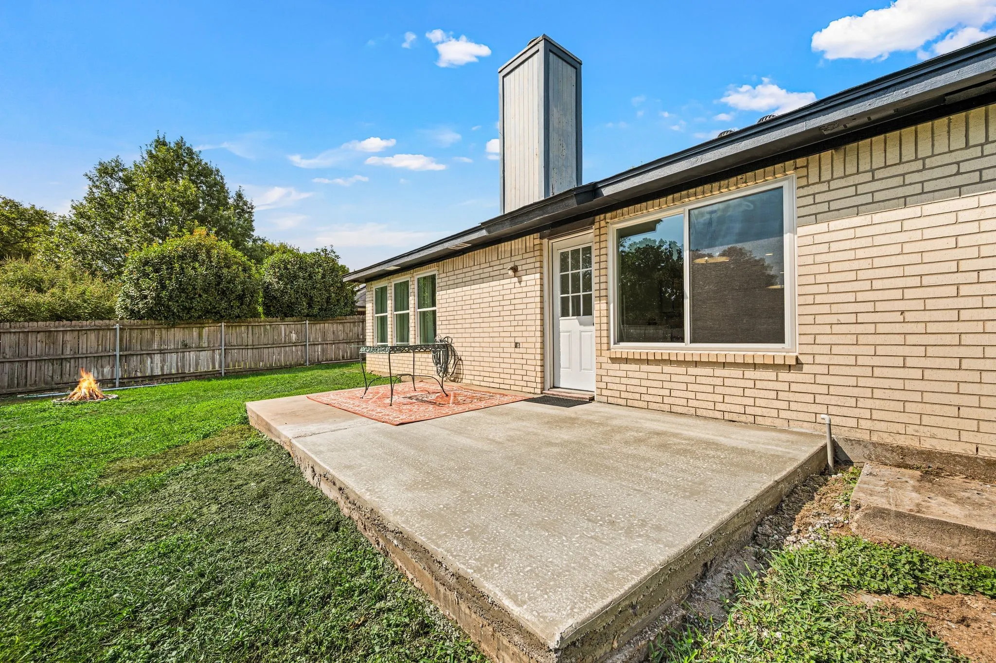 Brick exterior with a concrete patio, fenced backyard, and a prominent chimney feature