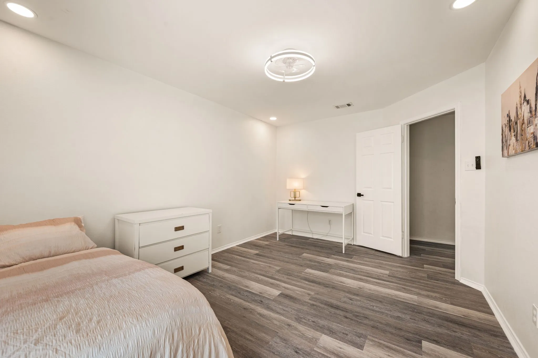 Recessed lighting, wood-finish flooring, white walls, and a white panel door with black hardware