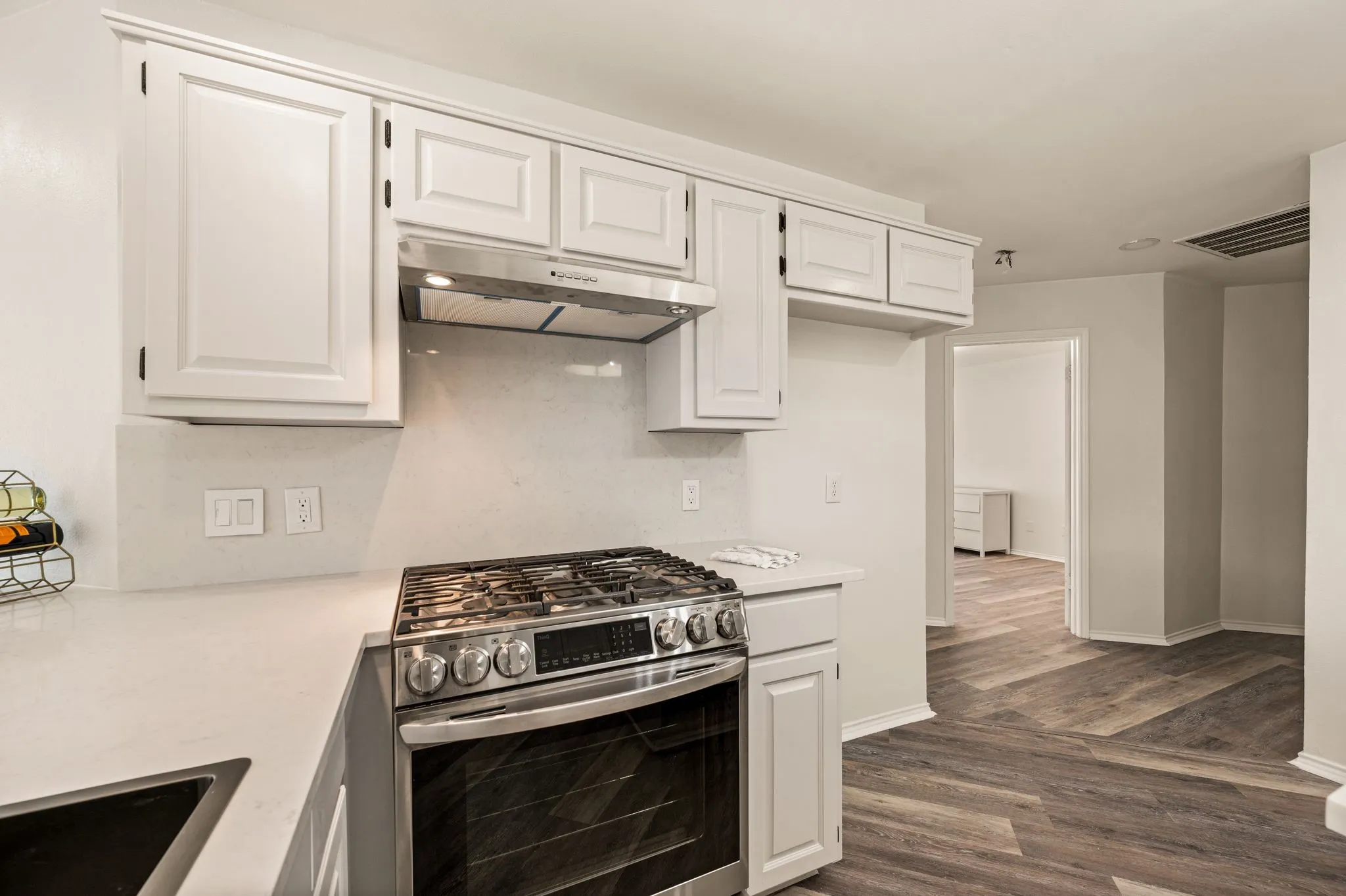 Kitchen featuring white cabinetry, light countertops, stainless steel range with gas burners, and a coordinating stainless steel range hood
