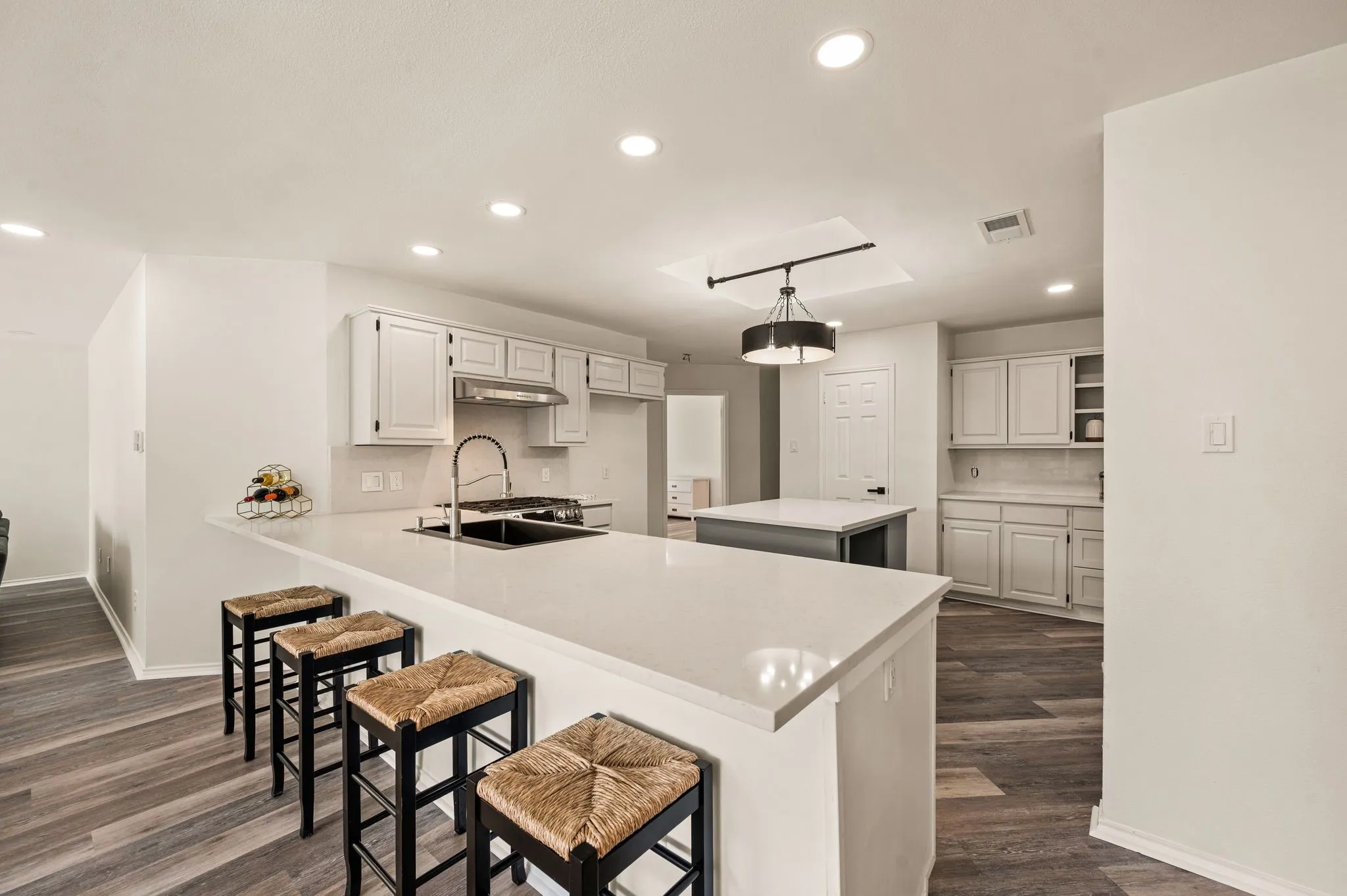 Kitchen featuring white cabinetry, a central island, a large breakfast bar with light-toned countertops, and wood-finish flooring