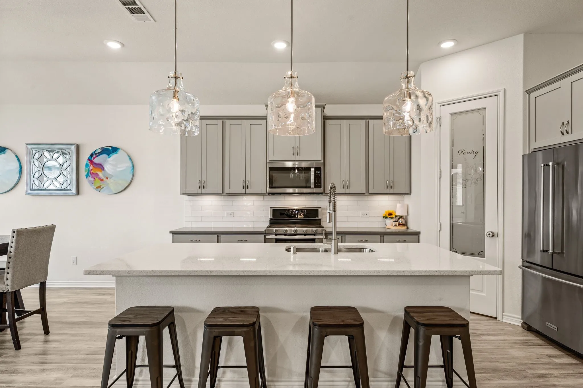 Kitchen featuring a wonderfully sized island with quartz  countertop, stainless steel appliances, grey cabinetry, LTV flooring and fabulous pendant lighting to make your kitchen even more spectacular!