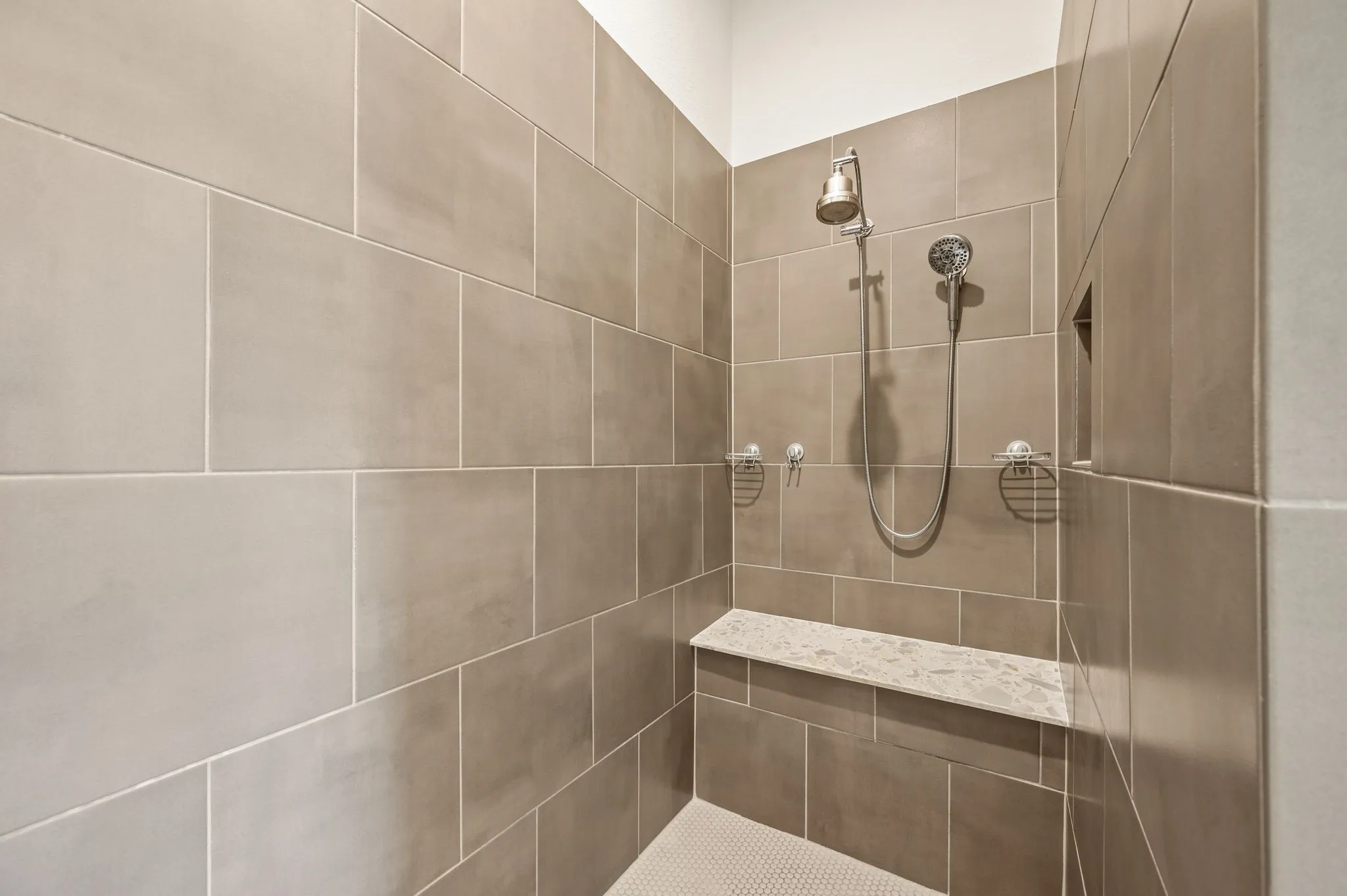 Over sized stand alone Shower featuring large wall tiling, a built-in shower bench with a stone top, and a recessed niche, tow shoer heads and a spa like shower to enjoy.