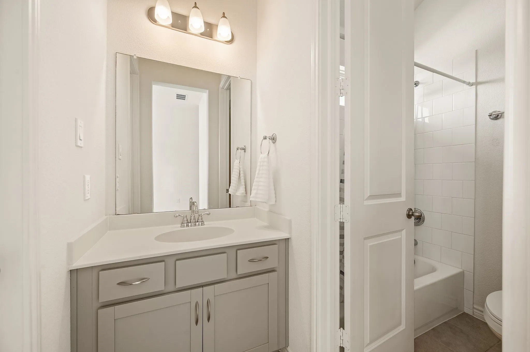 Light gray vanity with brushed nickel hardware, white countertop, and integrated sink that has a Jack and Jill bathroom.