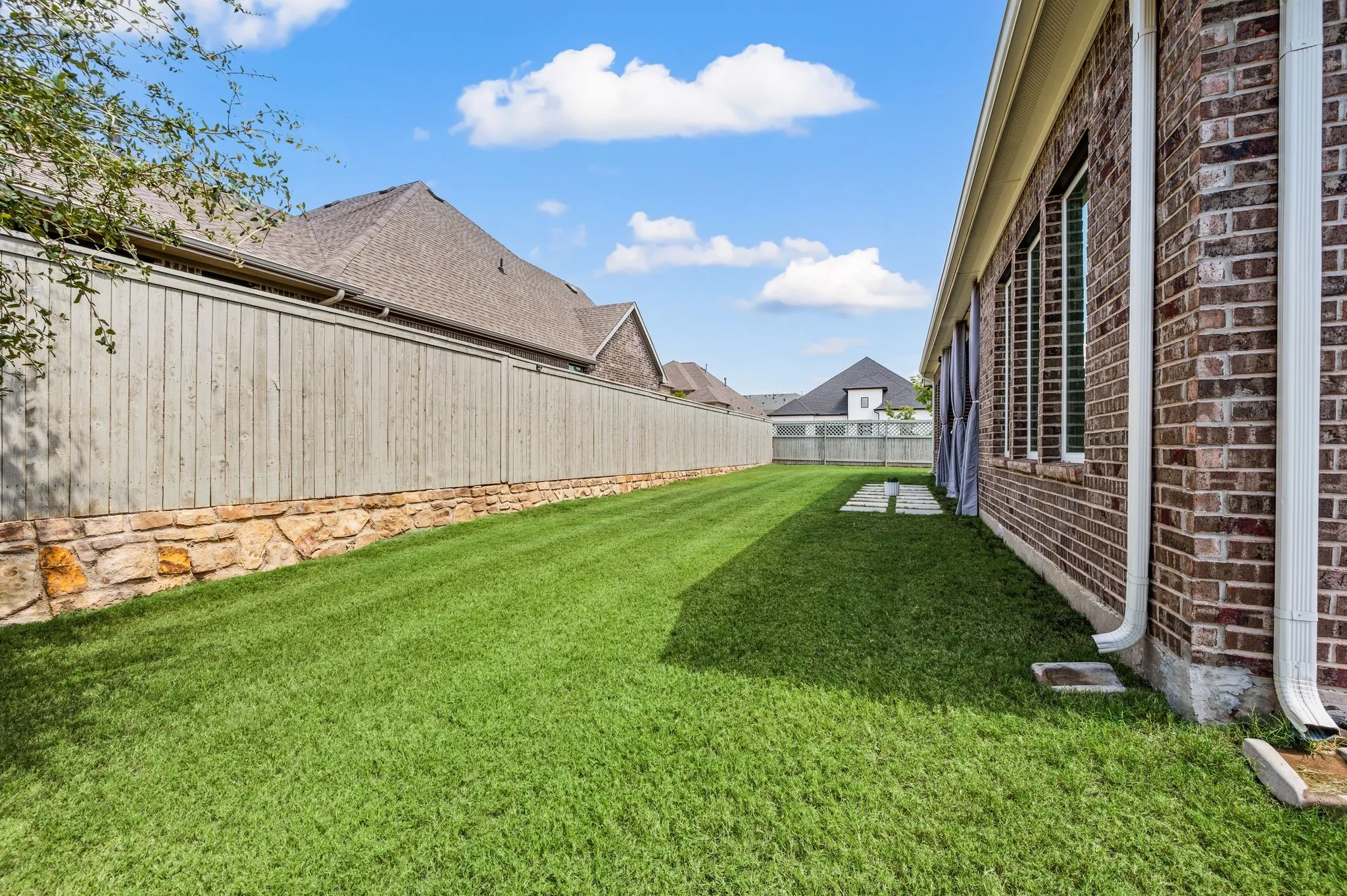 Expansive lawn area featuring a stone and wood privacy fence, and some stone pavers to even extend the patio out a little bit more!