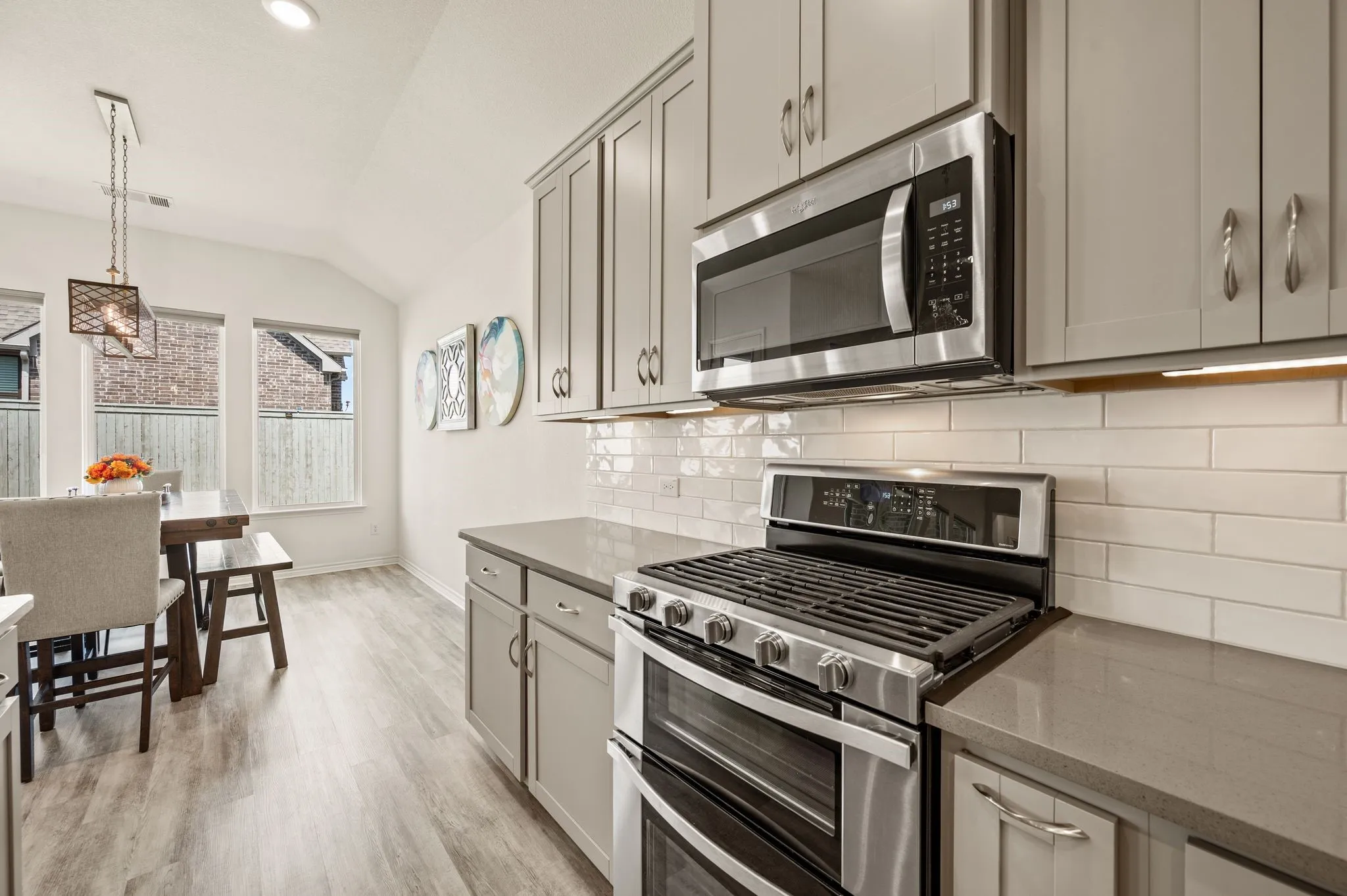 Contemporary kitchen featuring stainless steel appliances, grey cabinetry, light-toned quartz countertops, subway tile backsplash, and LTV flooring