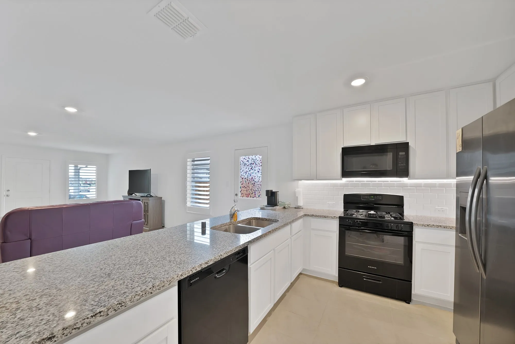 Kitchen featuring white shaker cabinetry, speckled countertops, stainless steel appliances, and a subway tile backsplash
