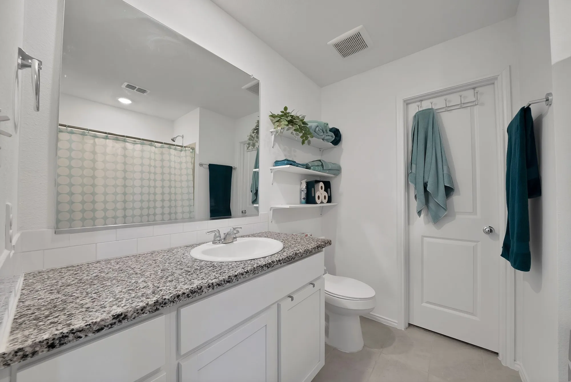 Vanity with a speckled countertop and integrated sink, white subway tile backsplash, full-width mirror, white paneled cabinetry, and a toilet