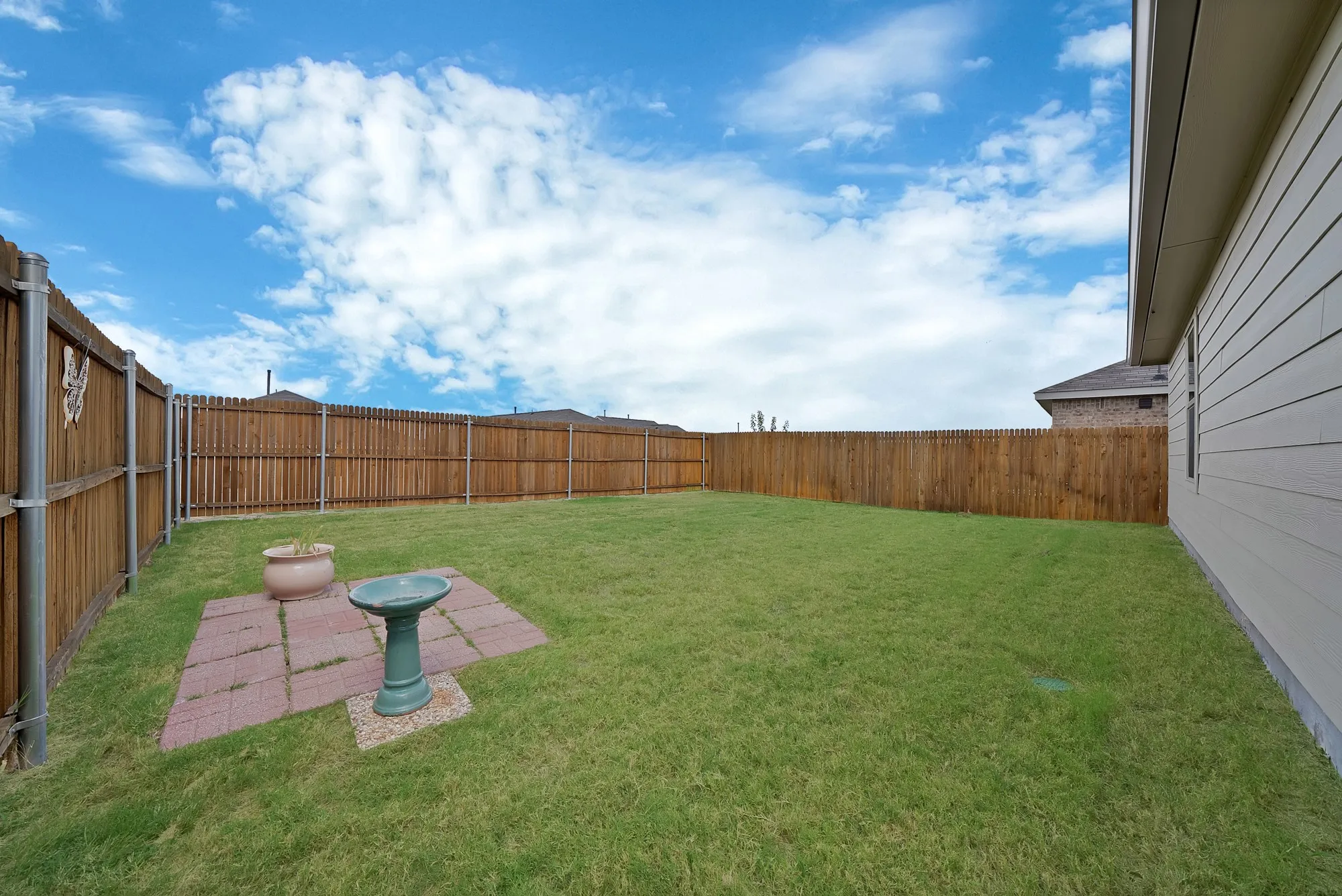 Expansive grassy backyard featuring a wood privacy fence, concrete slab foundation, and a small paved patio area