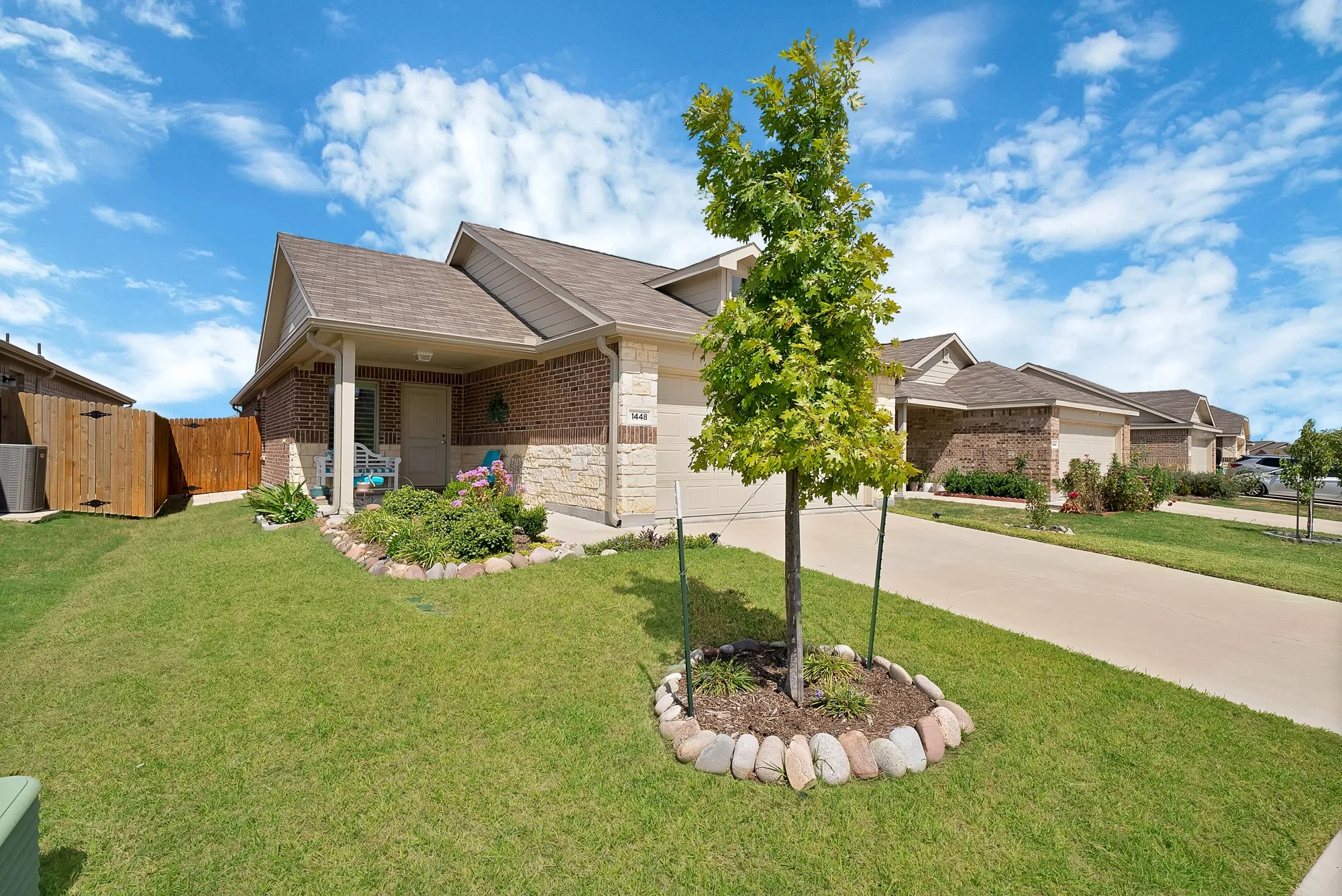 Brick and stone exterior with a covered front porch, attached garage, and a fenced side yard