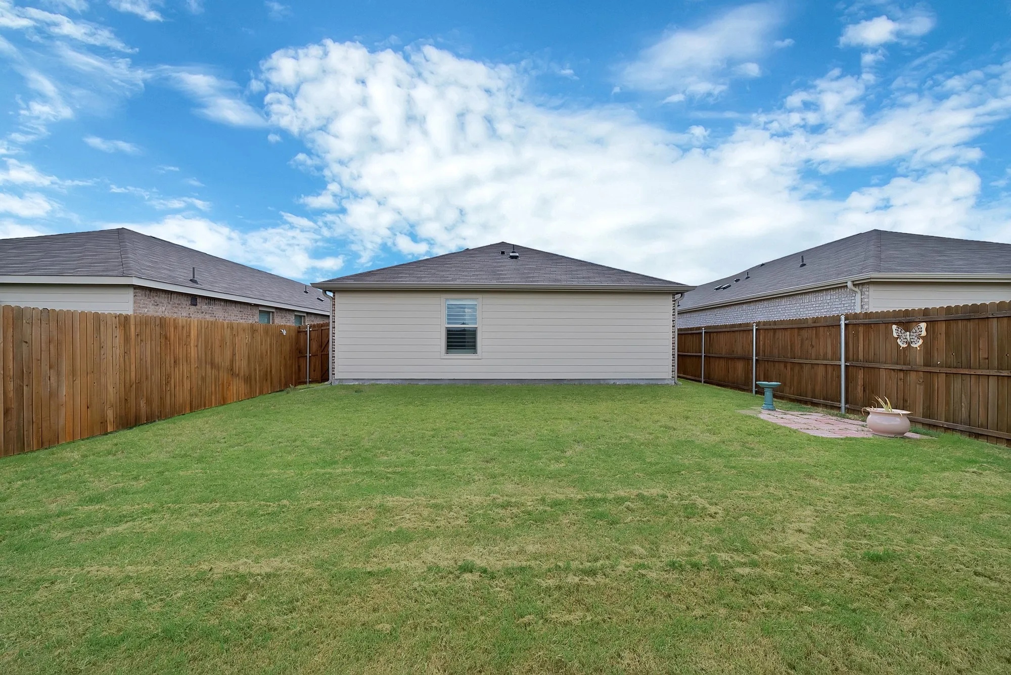 Expansive backyard with a manicured lawn, full wood fencing, and a central single-story dwelling