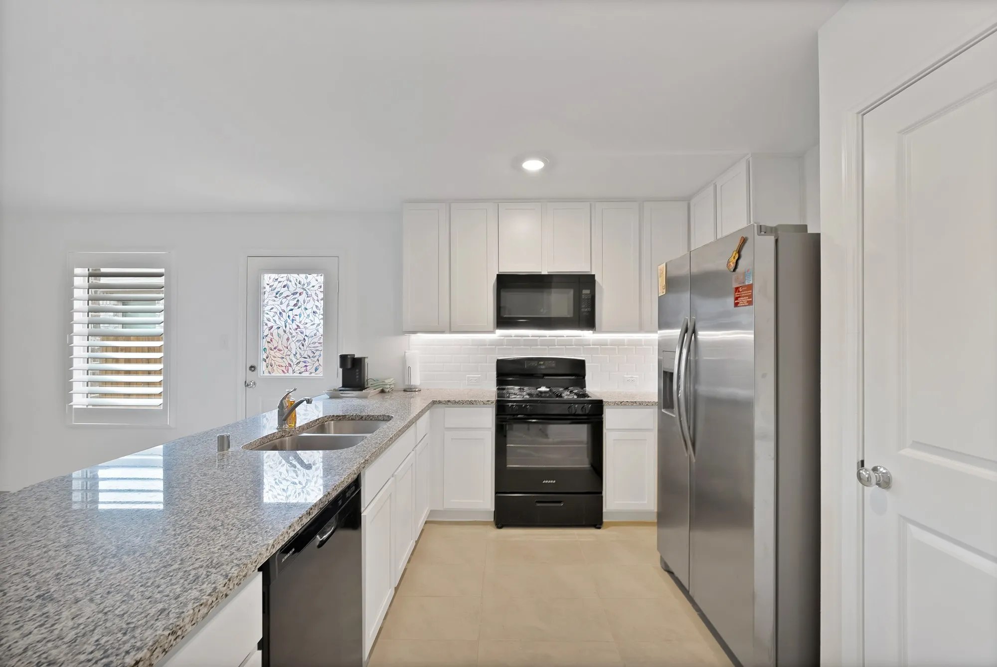 Kitchen featuring granite countertops, white cabinetry, a stainless steel refrigerator, a black gas range, and a white subway tile backsplash