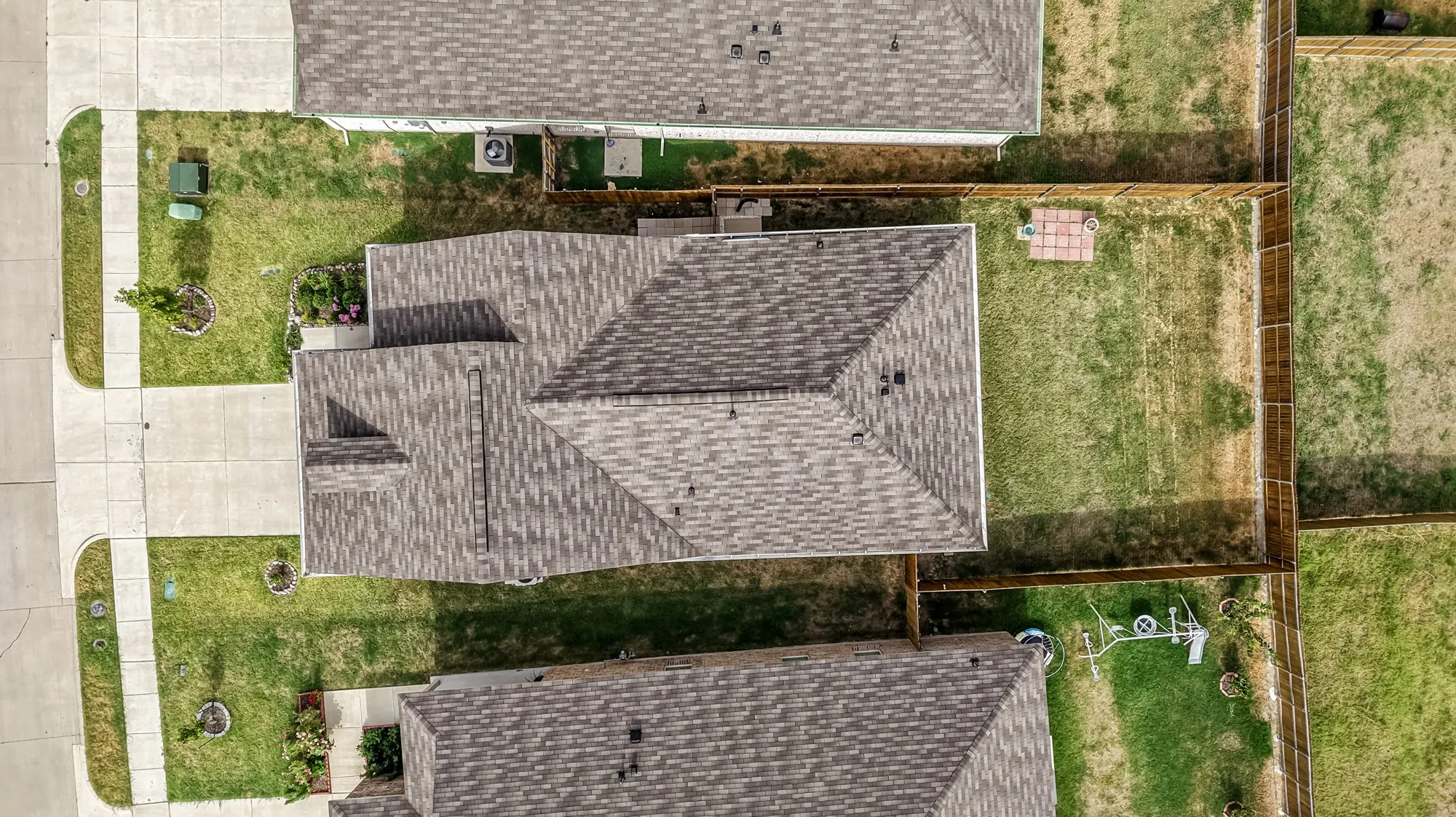 Pitched shingle roof, concrete driveway, concrete sidewalks, fenced backyard, and established lawn
