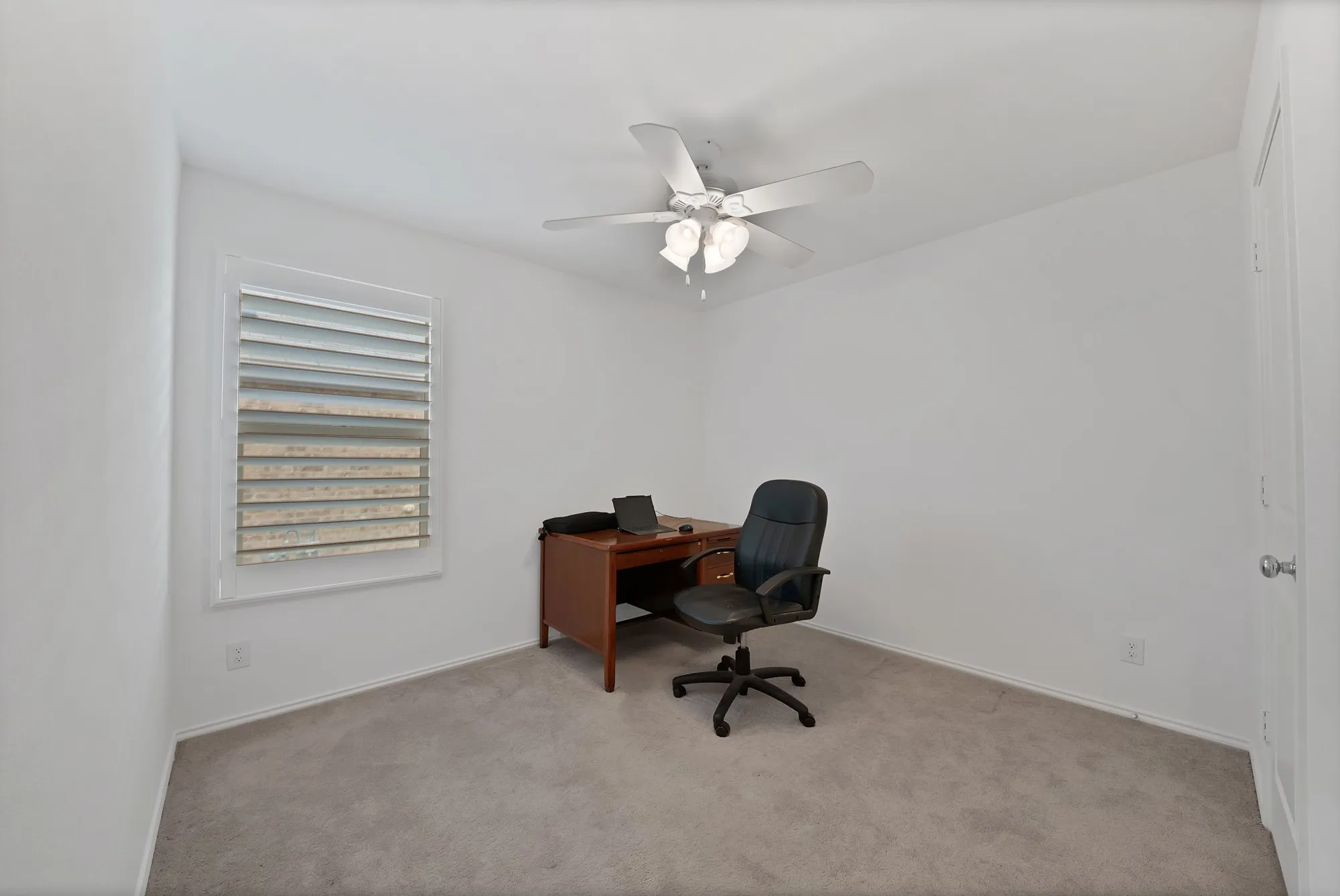 Neutral wall finishes with a ceiling fan light fixture, window with louvered shutters, and carpet flooring