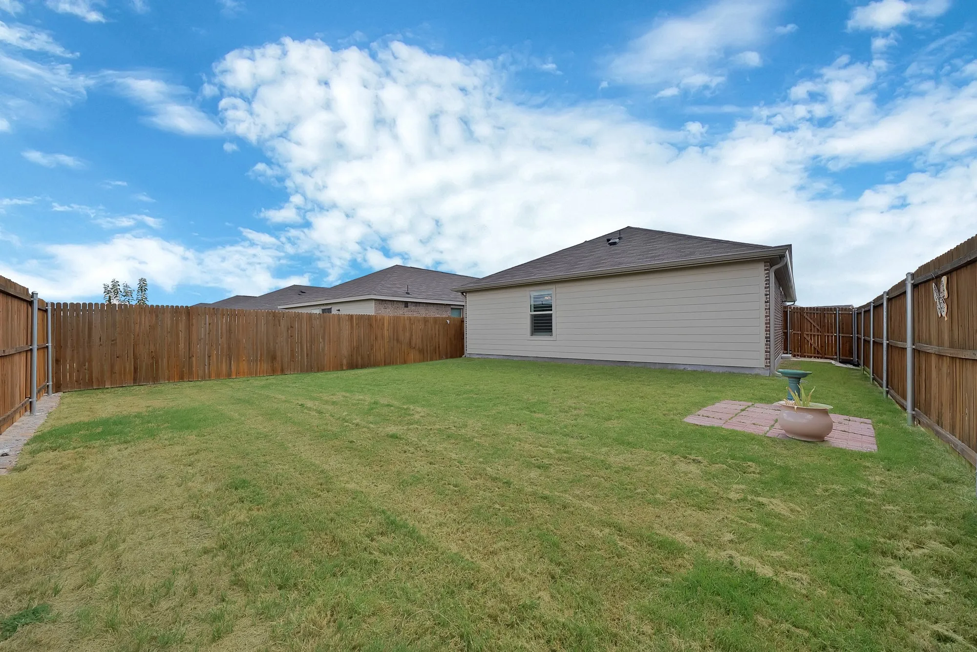 Expansive backyard featuring a wood privacy fence, a well-maintained lawn, and a small paver patio