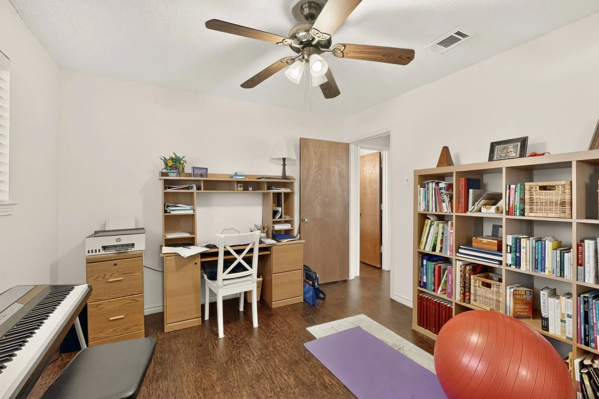 Wood-finish flooring, ceiling fan with integrated lighting, built-in shelving, white walls, and a window with blinds
