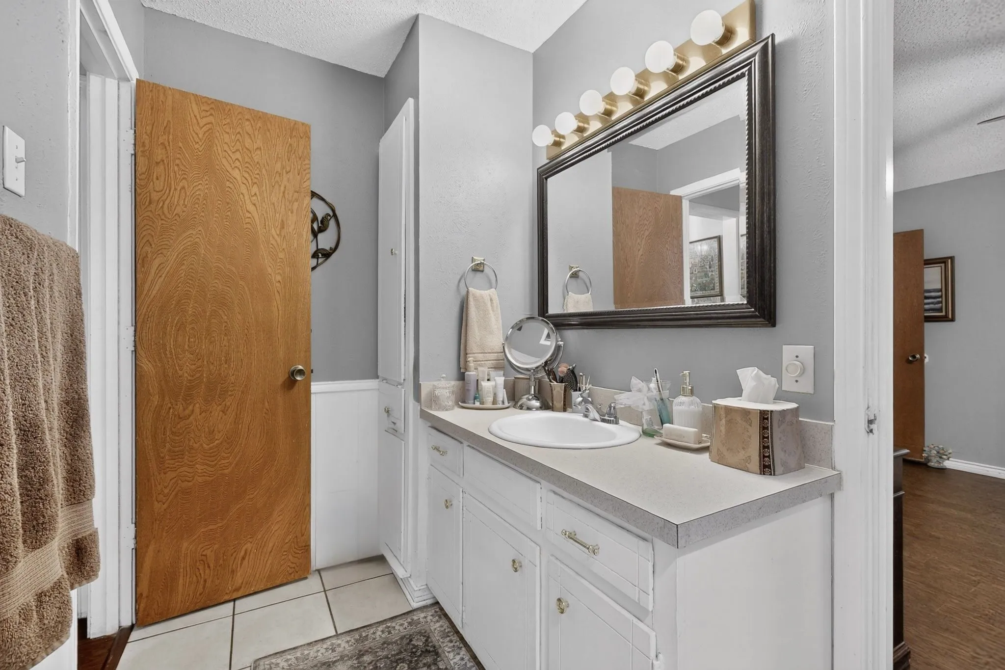 White vanity with a single basin sink, light-toned countertop, and recessed paneled cabinetry